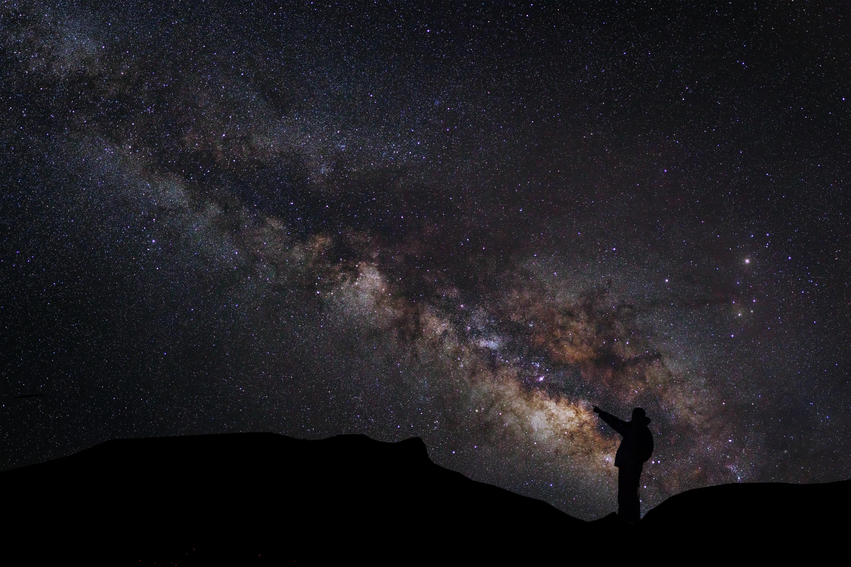 A Man is standing next to the milky way galaxy pointing on a bright star, Long exposure photograph, with grain Stock Free