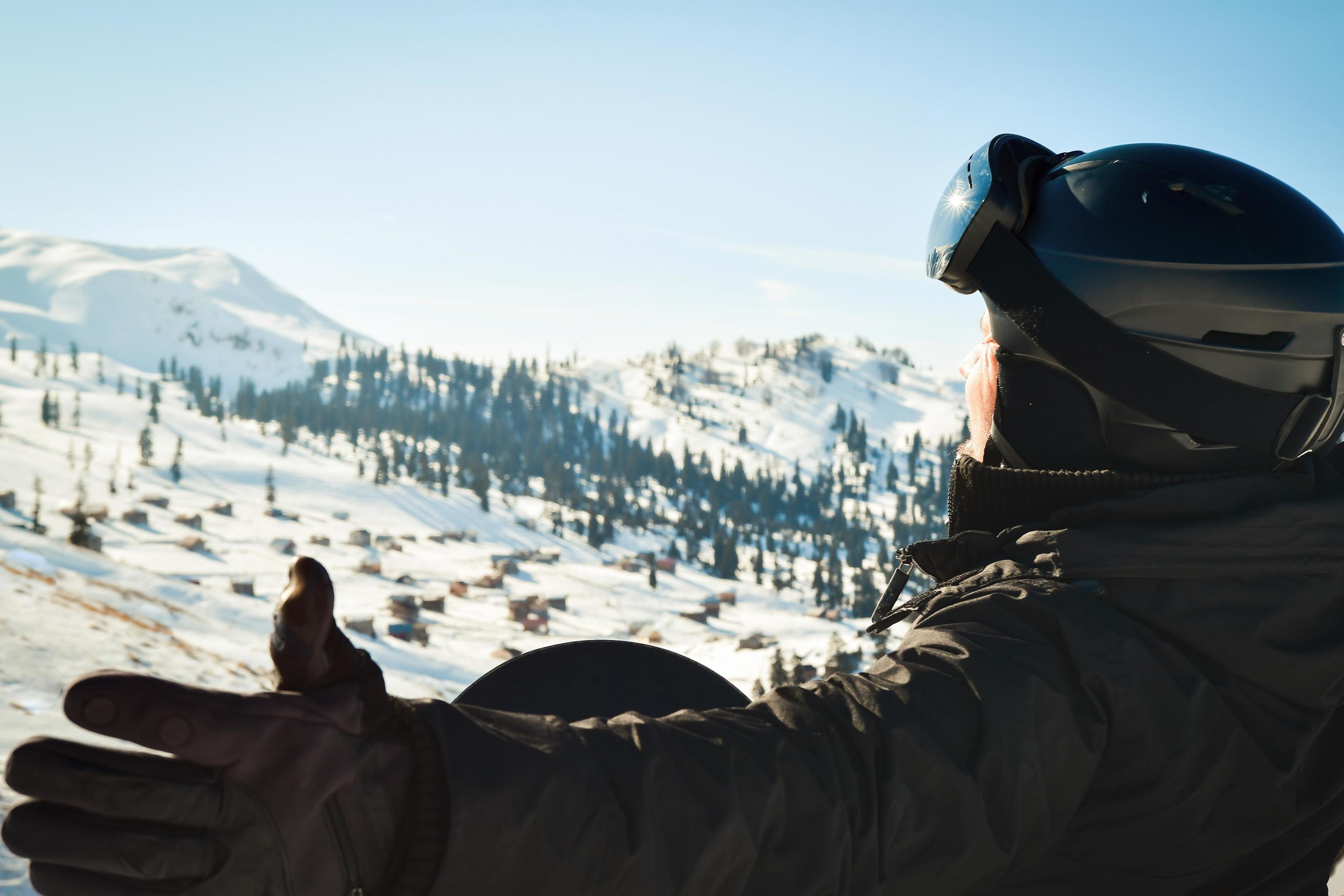 Male person alone in winter skiing outfit exited enjoys panorama of mountains with spreaded hands. Snowboard in forest and caucasus mountains Stock Free