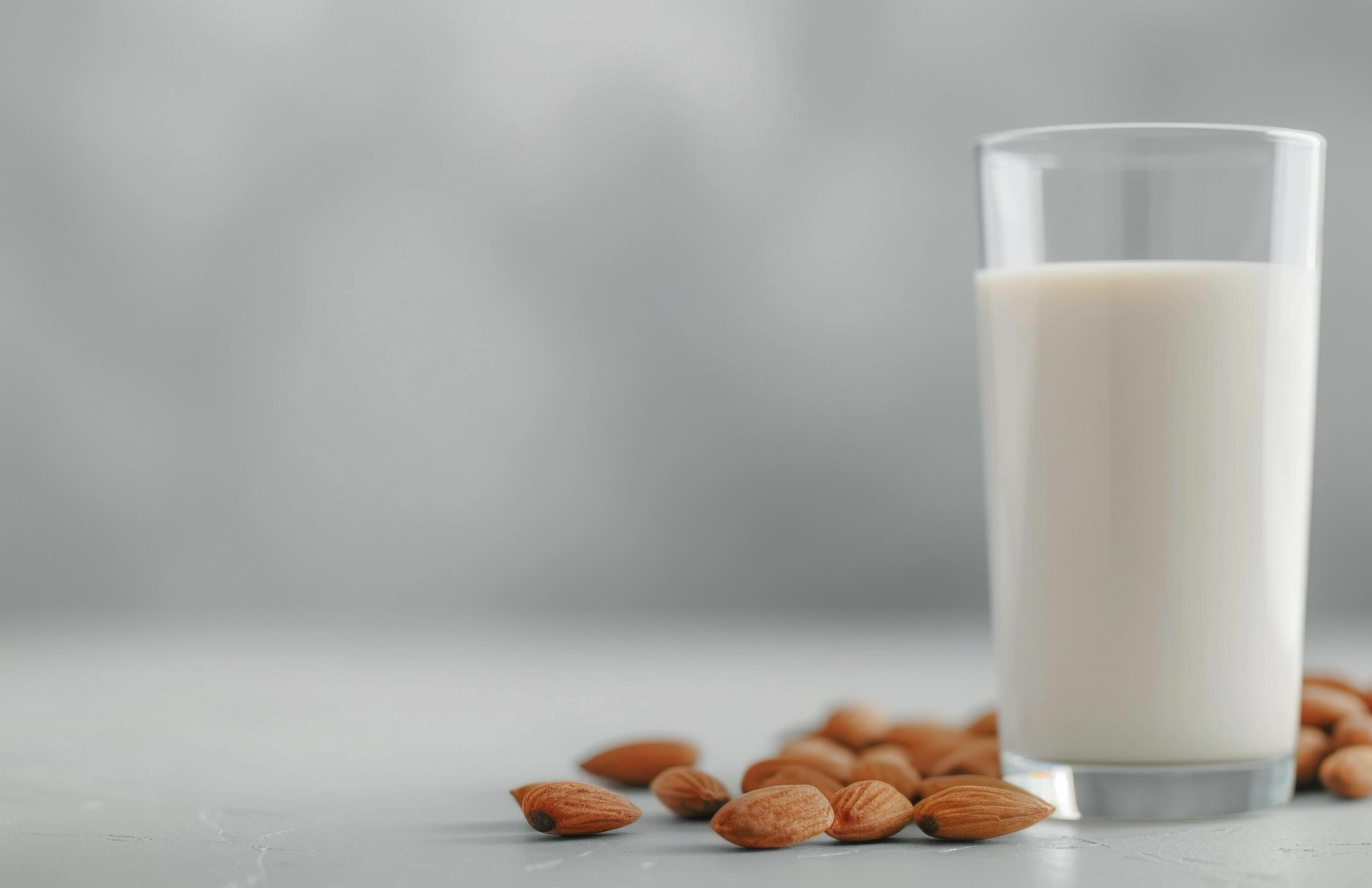 Creamy Almond Milk Surrounded by Almonds and Fresh Leaves on a White Background Stock Free