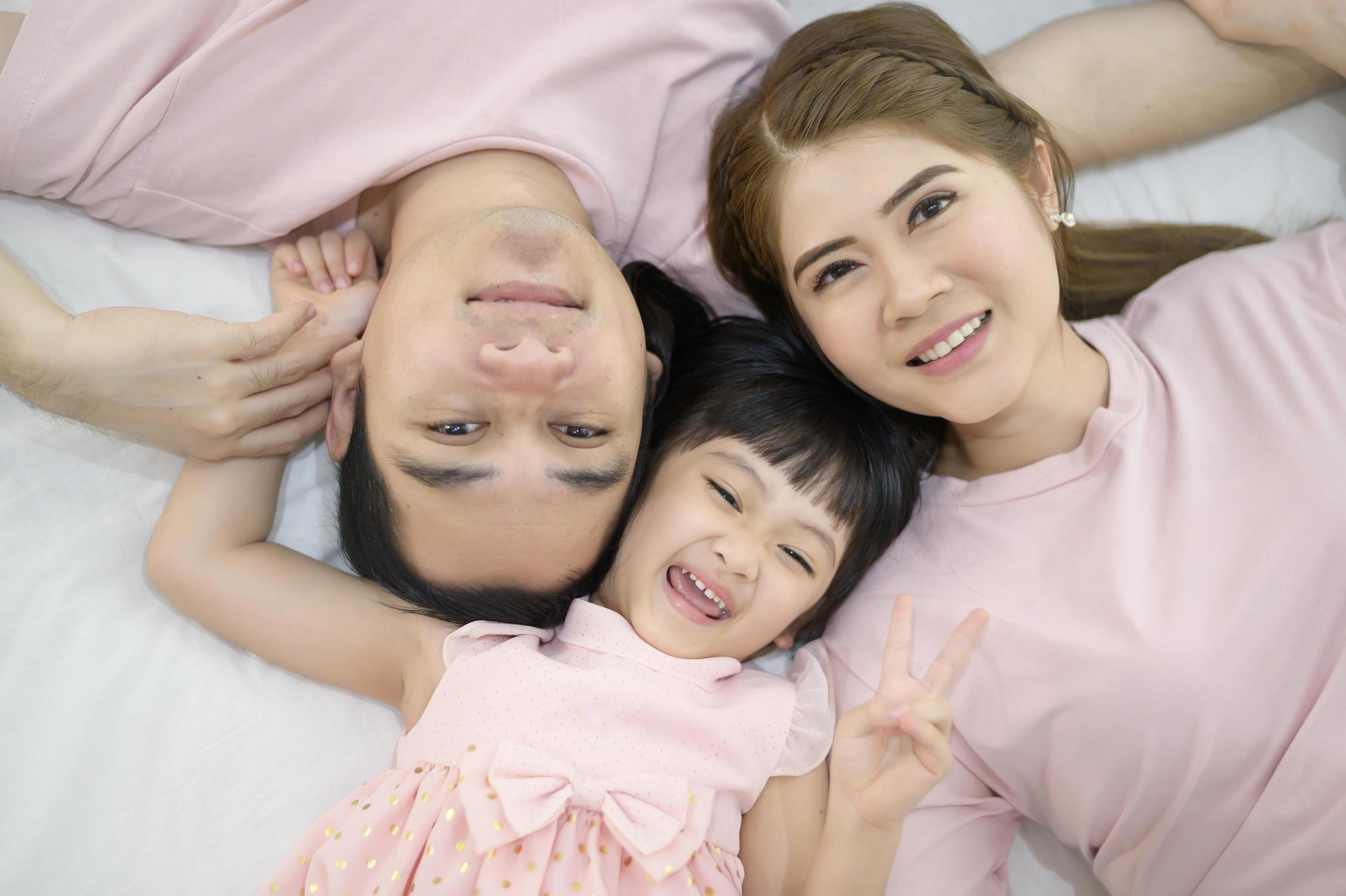 Top view of a happy asian family wearing pink shirt portrait on white bed indoor Stock Free