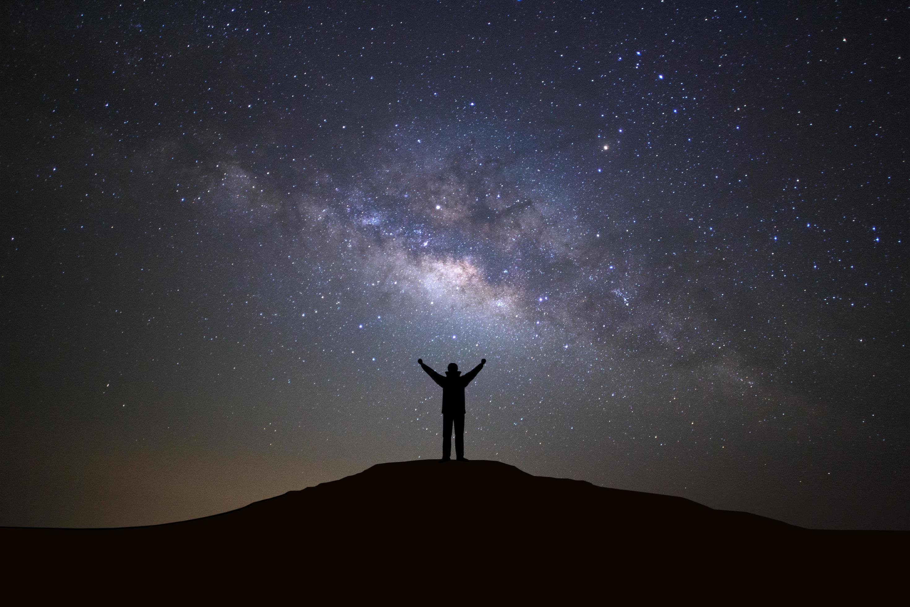 Landscape with milky way galaxy, Starry night sky with stars and silhouette of a standing sporty man with raised up arms on high mountain. Stock Free