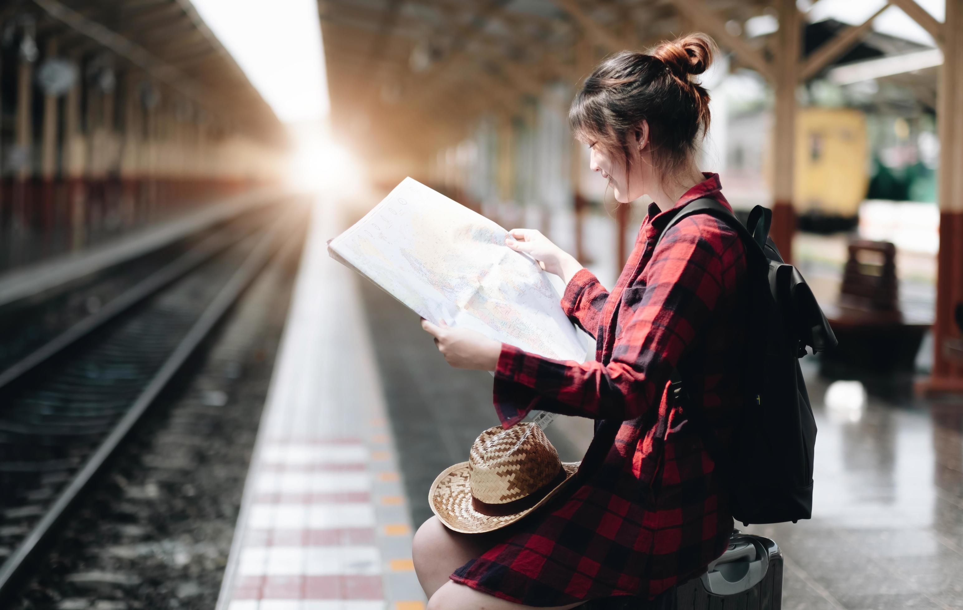 Pretty Young traveler woman looking on maps planning trip at public train station. Summer and travel lifestyle concept Stock Free