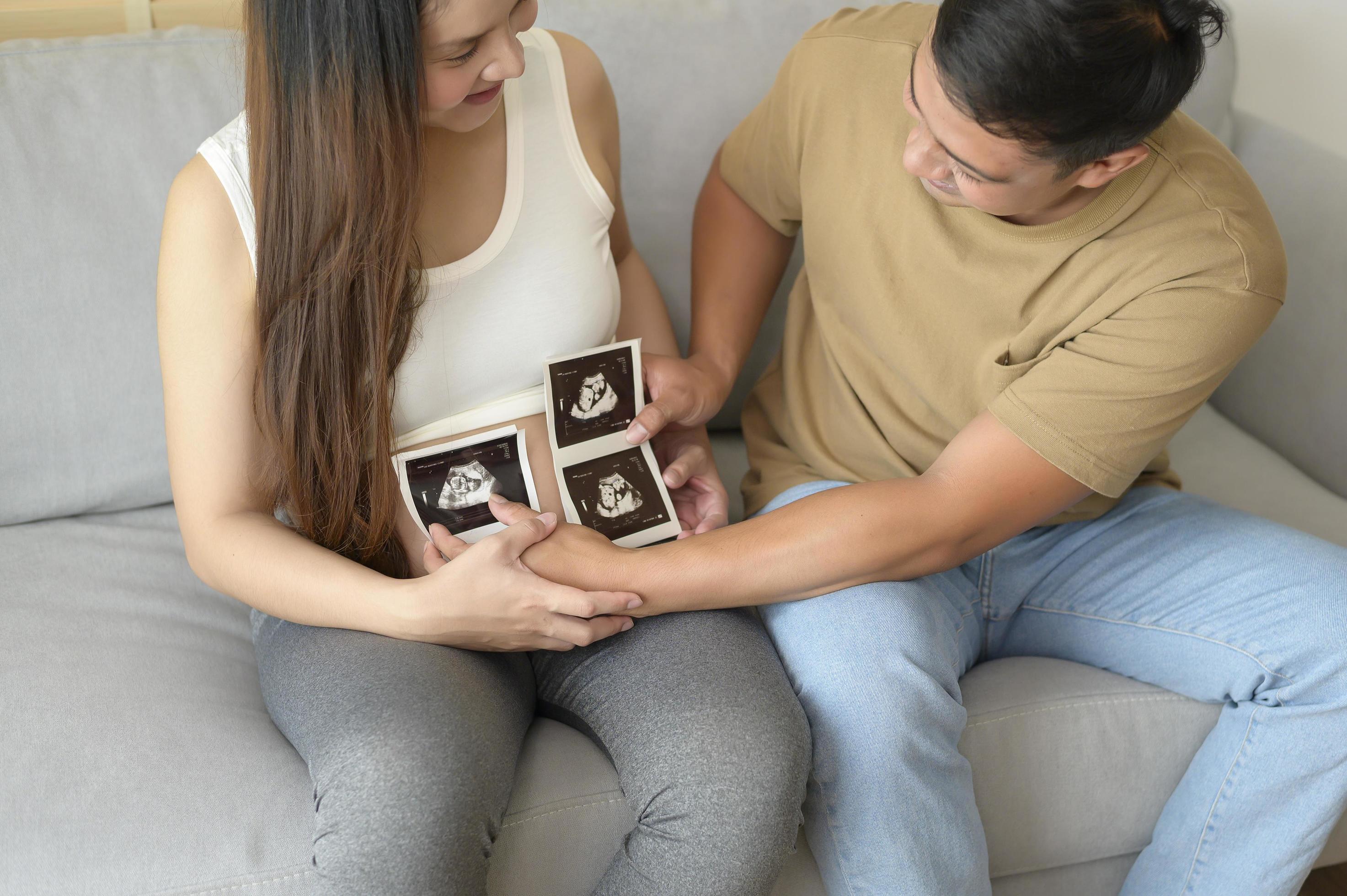 Young pregnant woman with husband holding ultrasound photo of newborn baby, maternity and family concept Stock Free