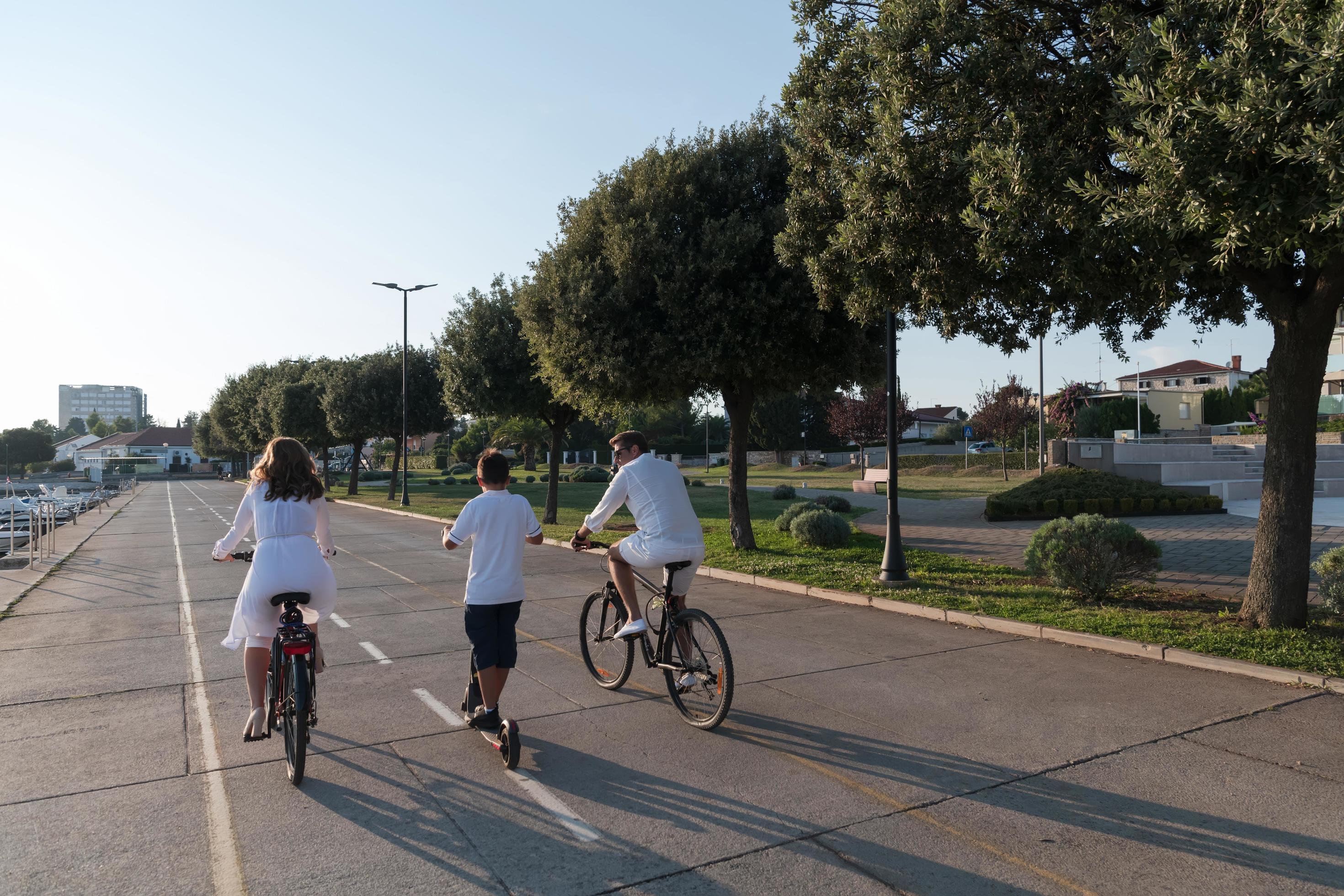 Happy family enjoying a beautiful morning by the sea together, parents riding a bike and their son riding an electric scooter. Selective focus Stock Free