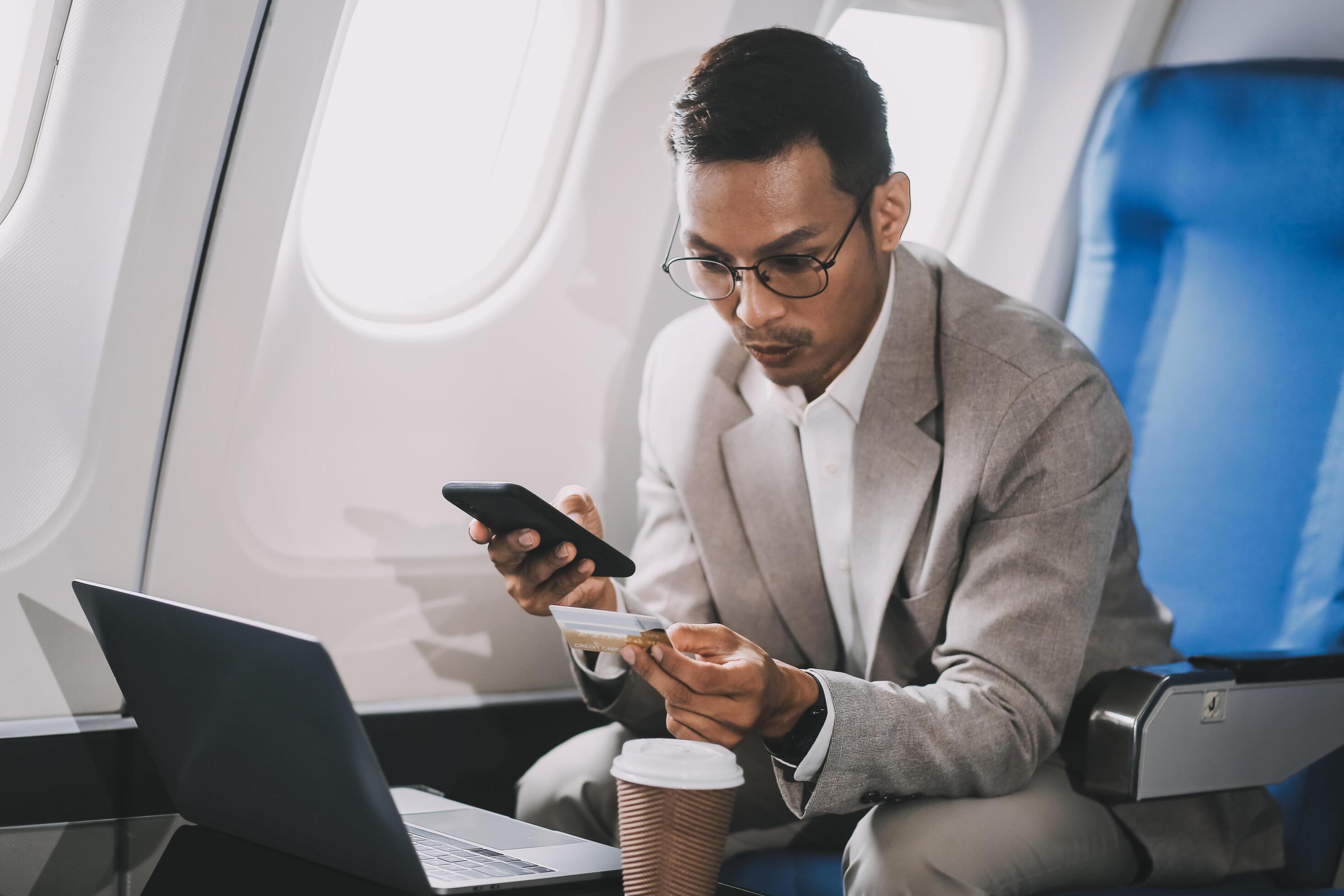 Businessman holding credit card and looking at camera near laptop in private jet Stock Free