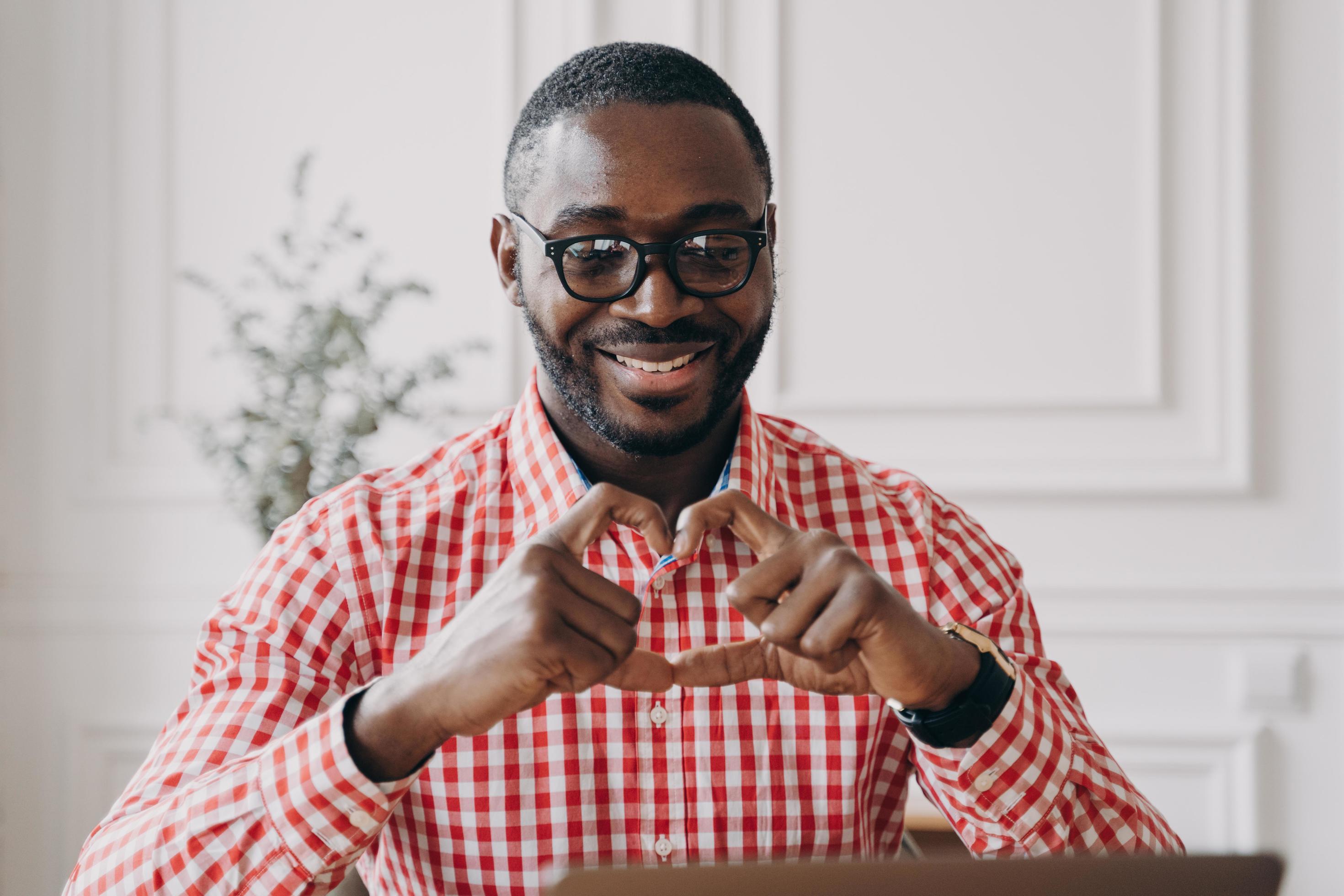 Happy african man gesturing heart symbol shape with hands during video call with family Stock Free