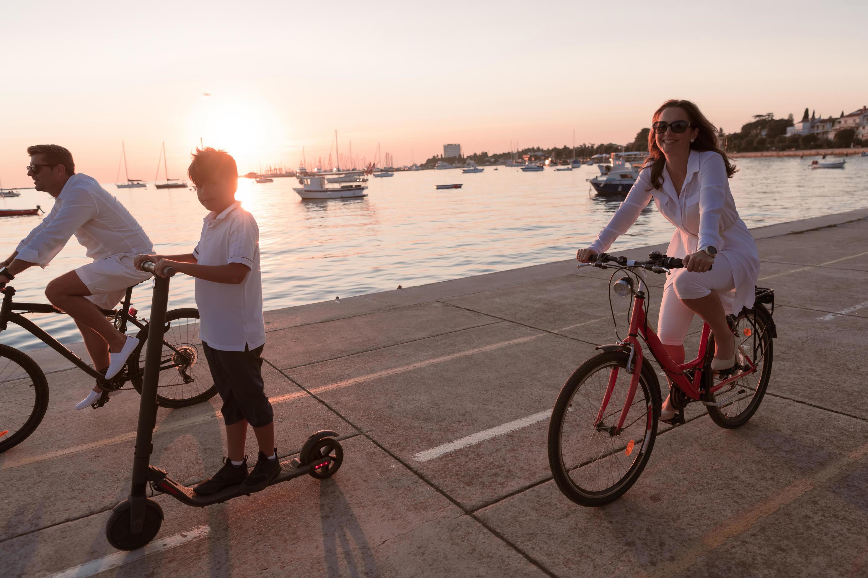 Happy family enjoying a beautiful morning by the sea together, parents riding a bike and their son riding an electric scooter. Selective focus Stock Free