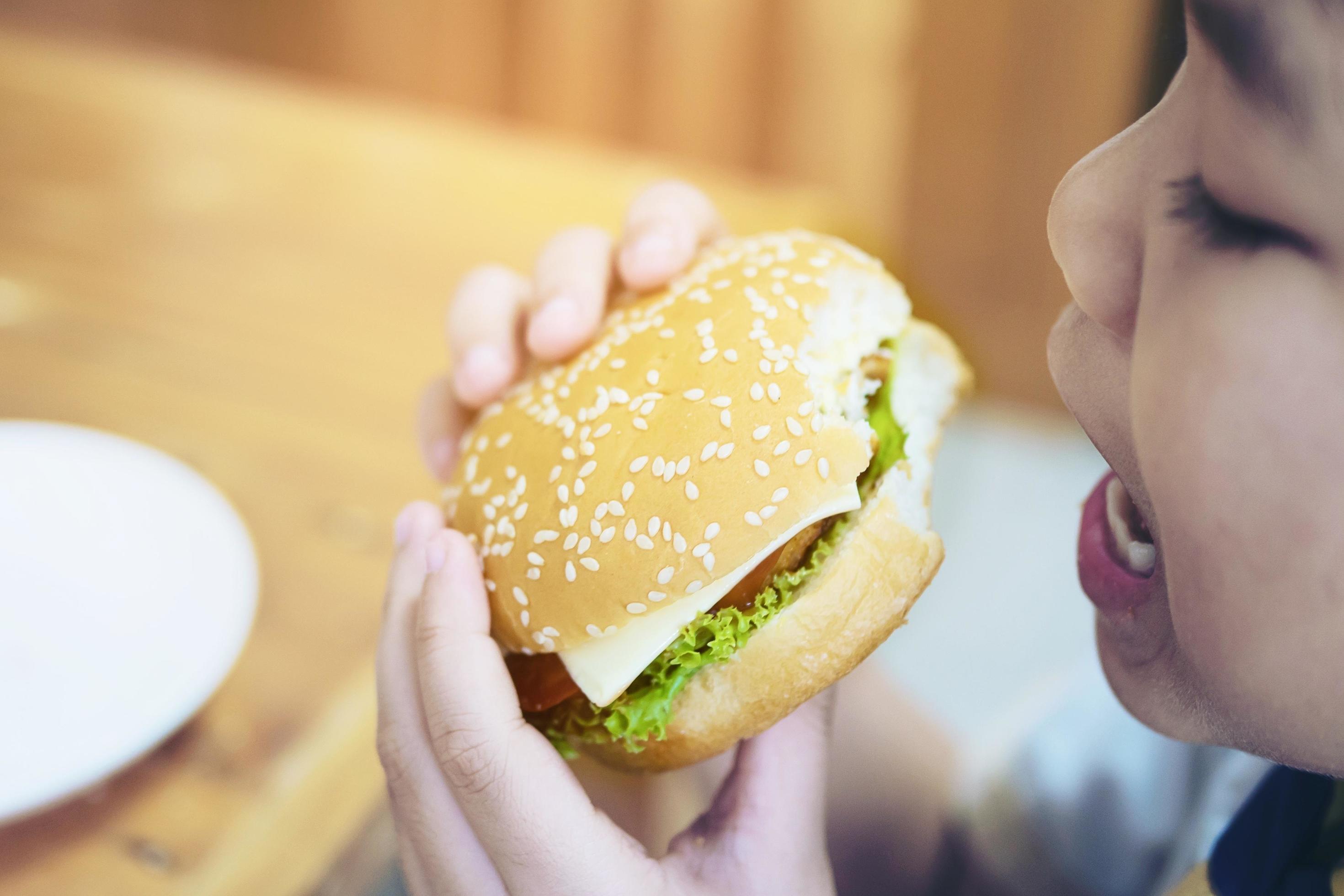 Boy eat hamburger breakfast with blur wooden table background – delicious fast food breakfast concept Stock Free