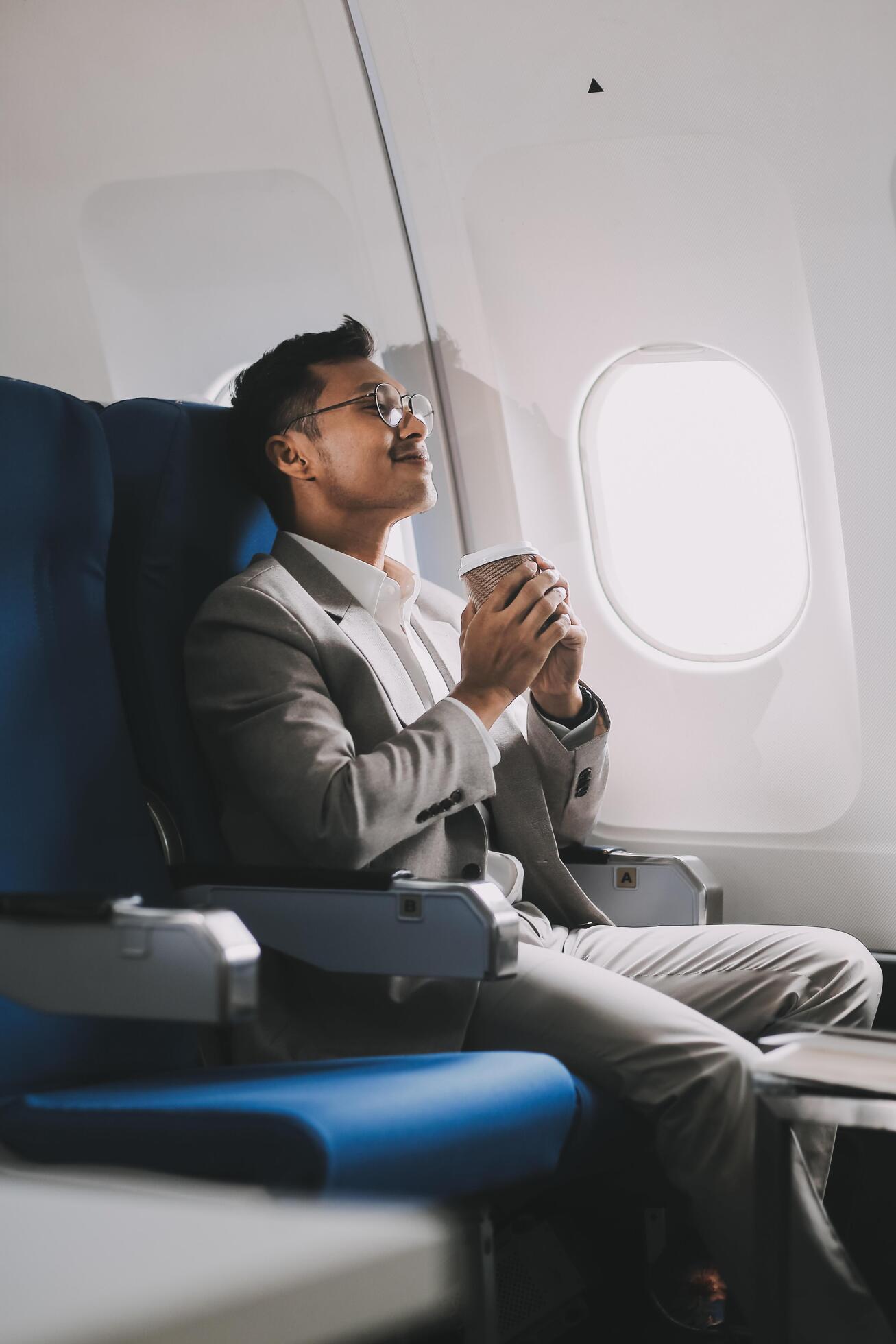 Asian businessman enjoying enjoys a coffee comfortable flight while sitting in the airplane cabin, Passengers near the window. Stock Free