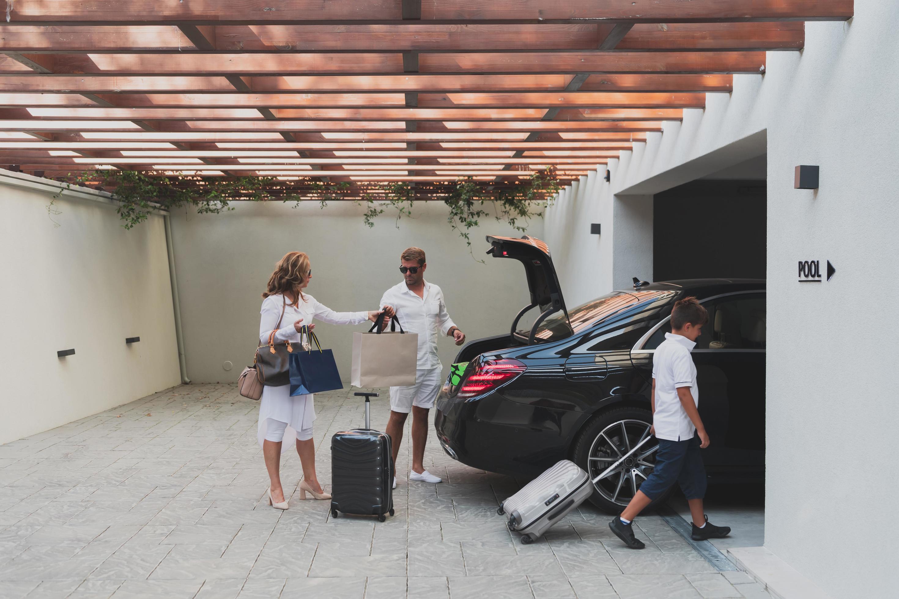 A photo of a modern family carrying suitcases from a garage to their luxury seaside home during a vacation. Vacation concept. Selective focus Stock Free