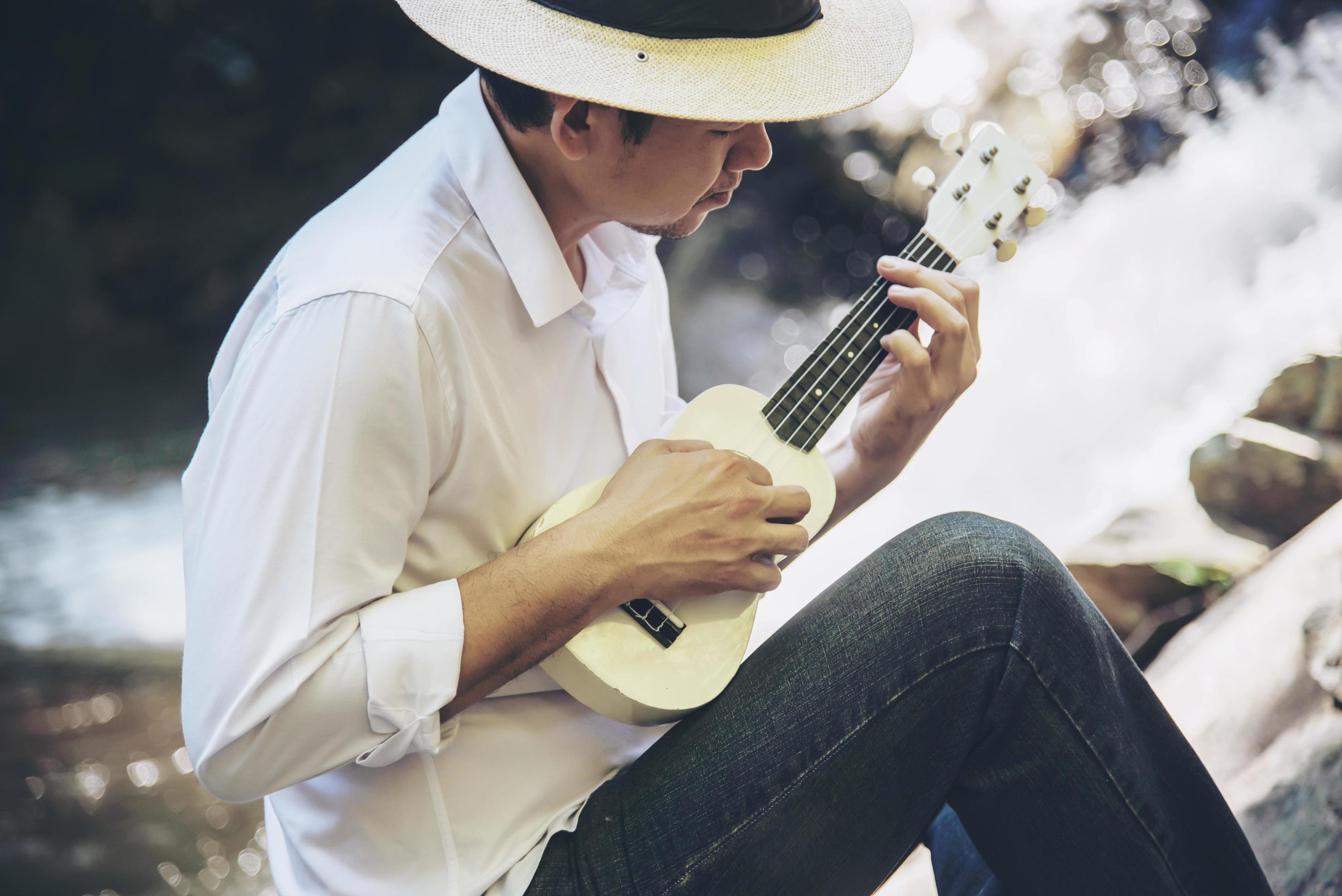 Man play ukulele new to the river- people and music instrument life style in nature concept Stock Free