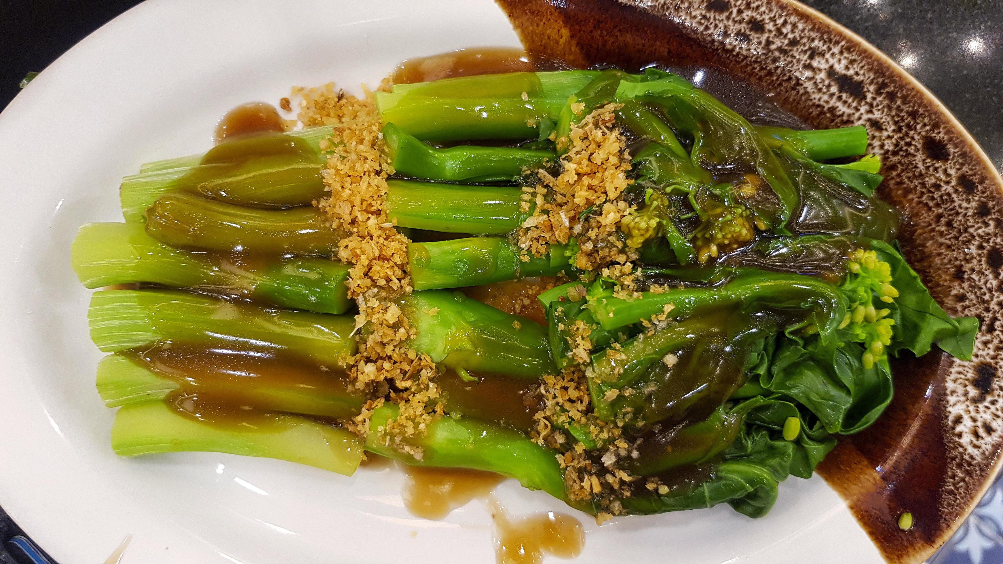 Hong Kong kale with oyster sauce and dried garlic topping on white dish or plate at Chinese restaurant. Delicious Asian food. Stock Free