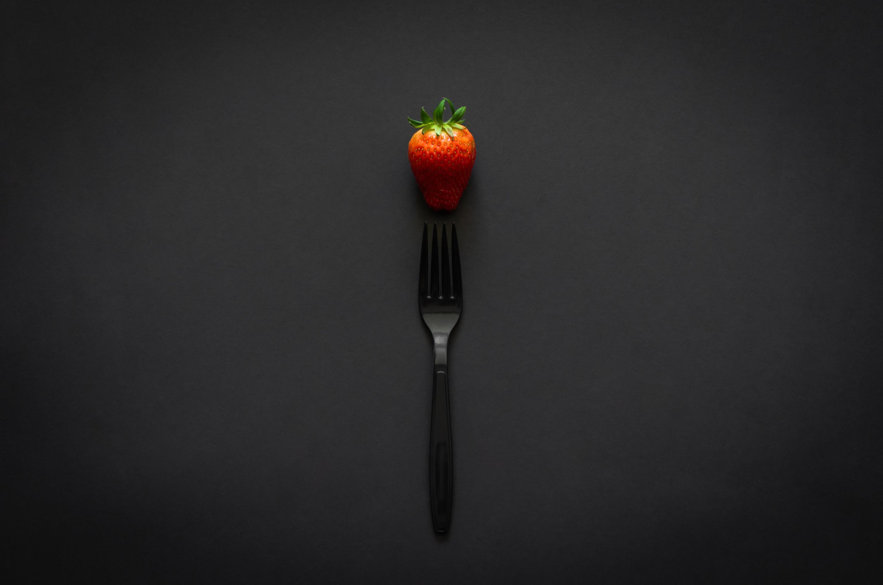 Strawberry and fork on dark background for minimalist flat lay black food concept. Stock Free