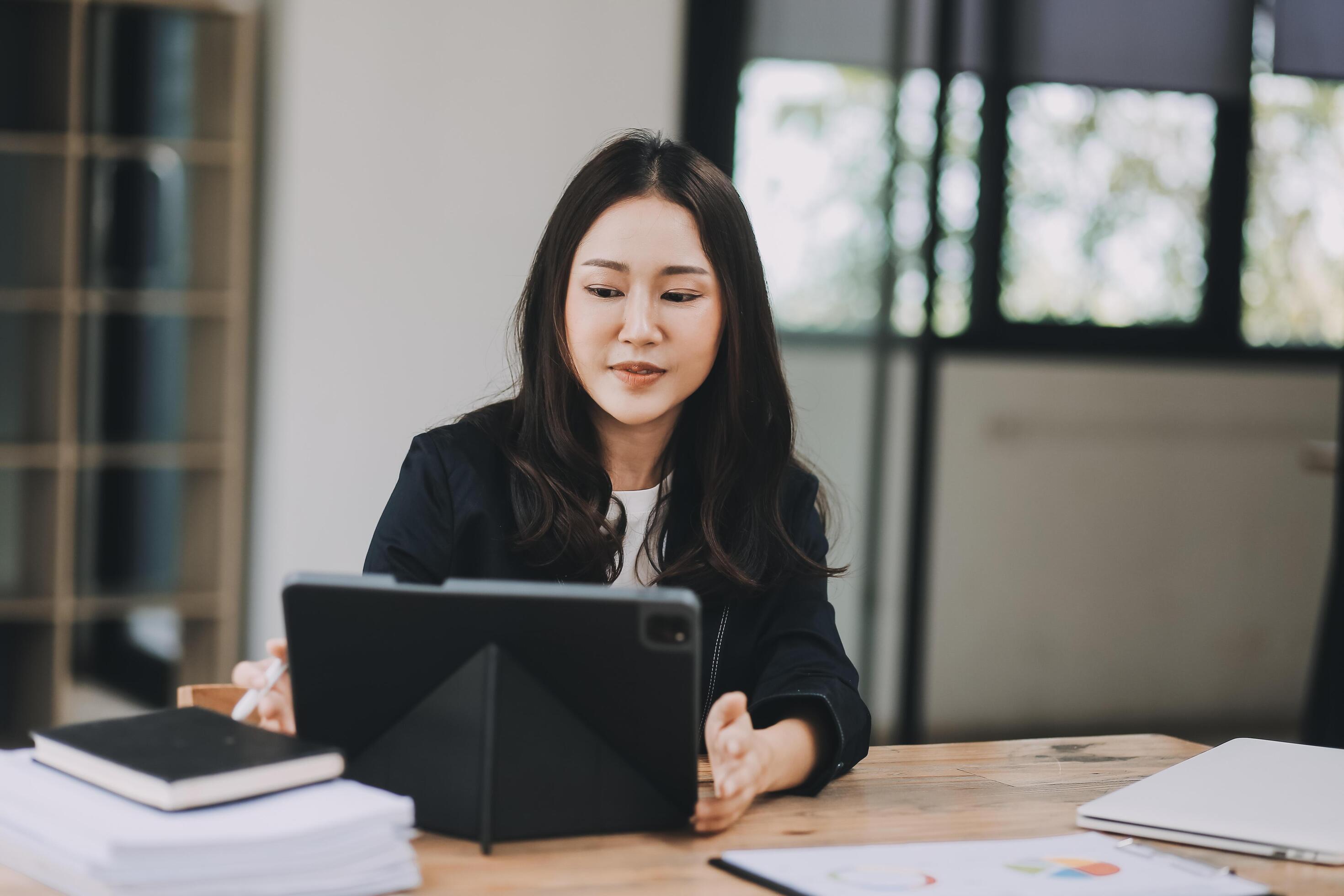 Pretty young Asian businesswoman working on laptop and taking notes In office. Stock Free