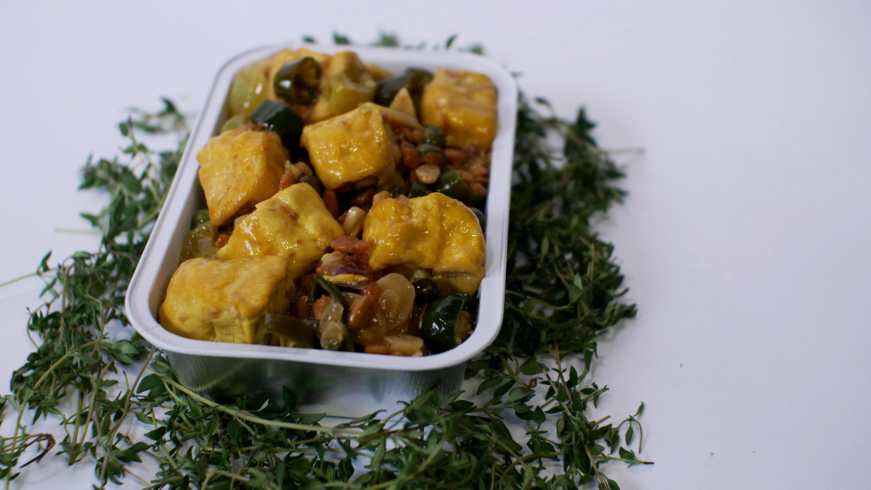 Vegetable tofu with yellow spices Indonesian food served in an aluminum holder with a white background with a few green leaves around it Stock Free