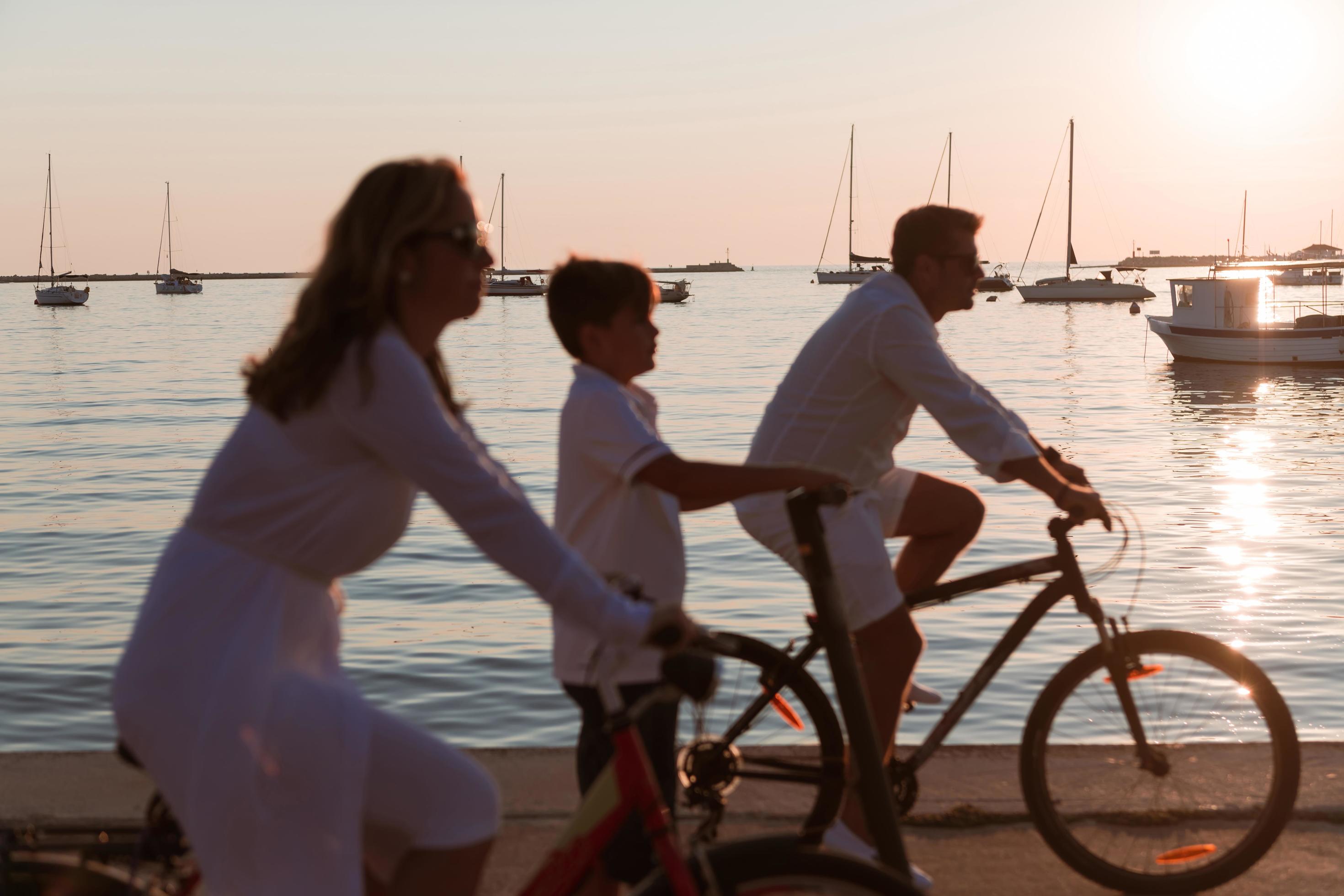 Happy family enjoying a beautiful morning by the sea together, parents riding a bike and their son riding an electric scooter. Selective focus Stock Free