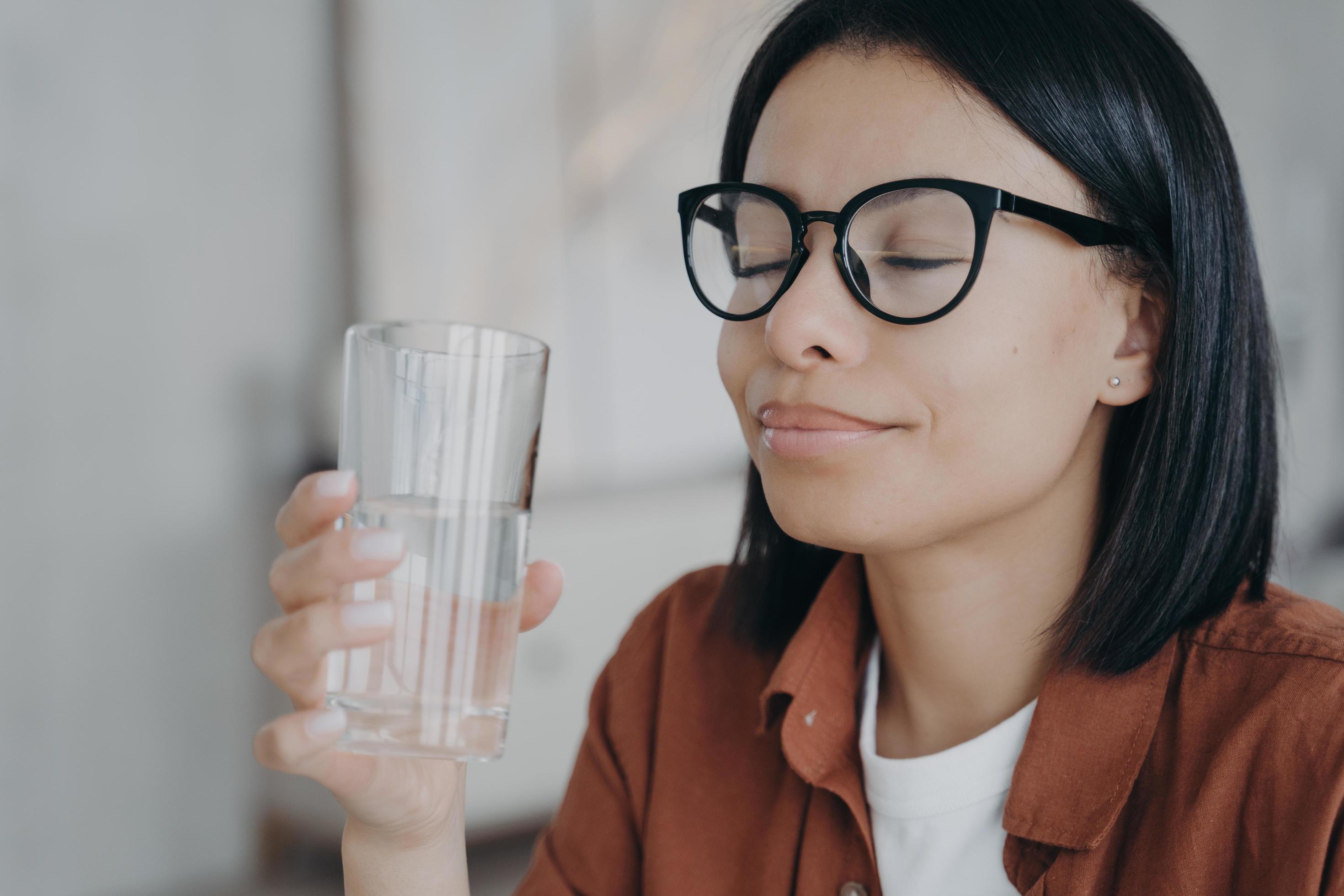 Happy woman wearing glasses holds glass of pure water, closed eyes. Healthy lifestyle, wellness Stock Free