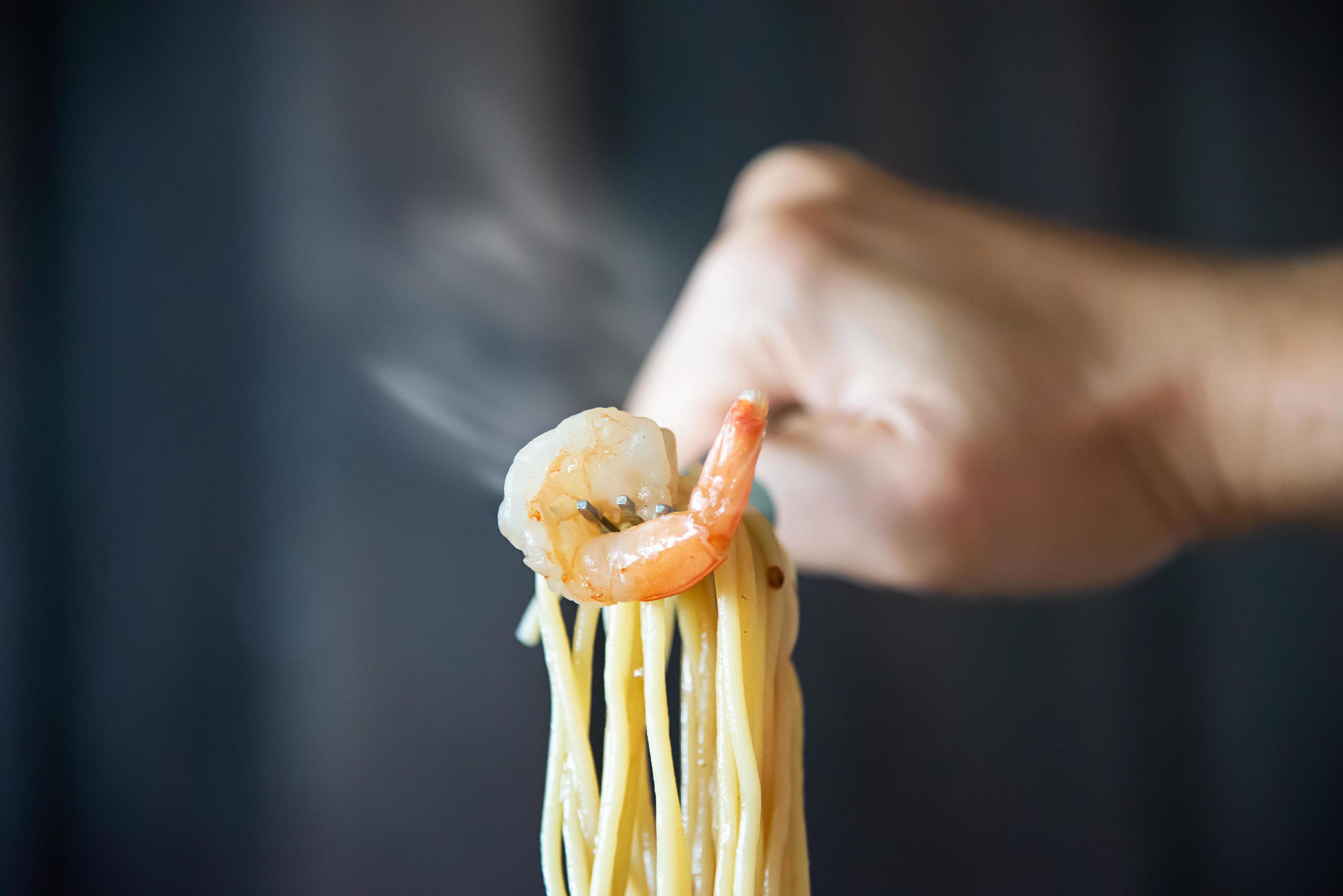 Hot and spicy spaghetti with shrimp and fork over black background – Italian food with people concept Stock Free