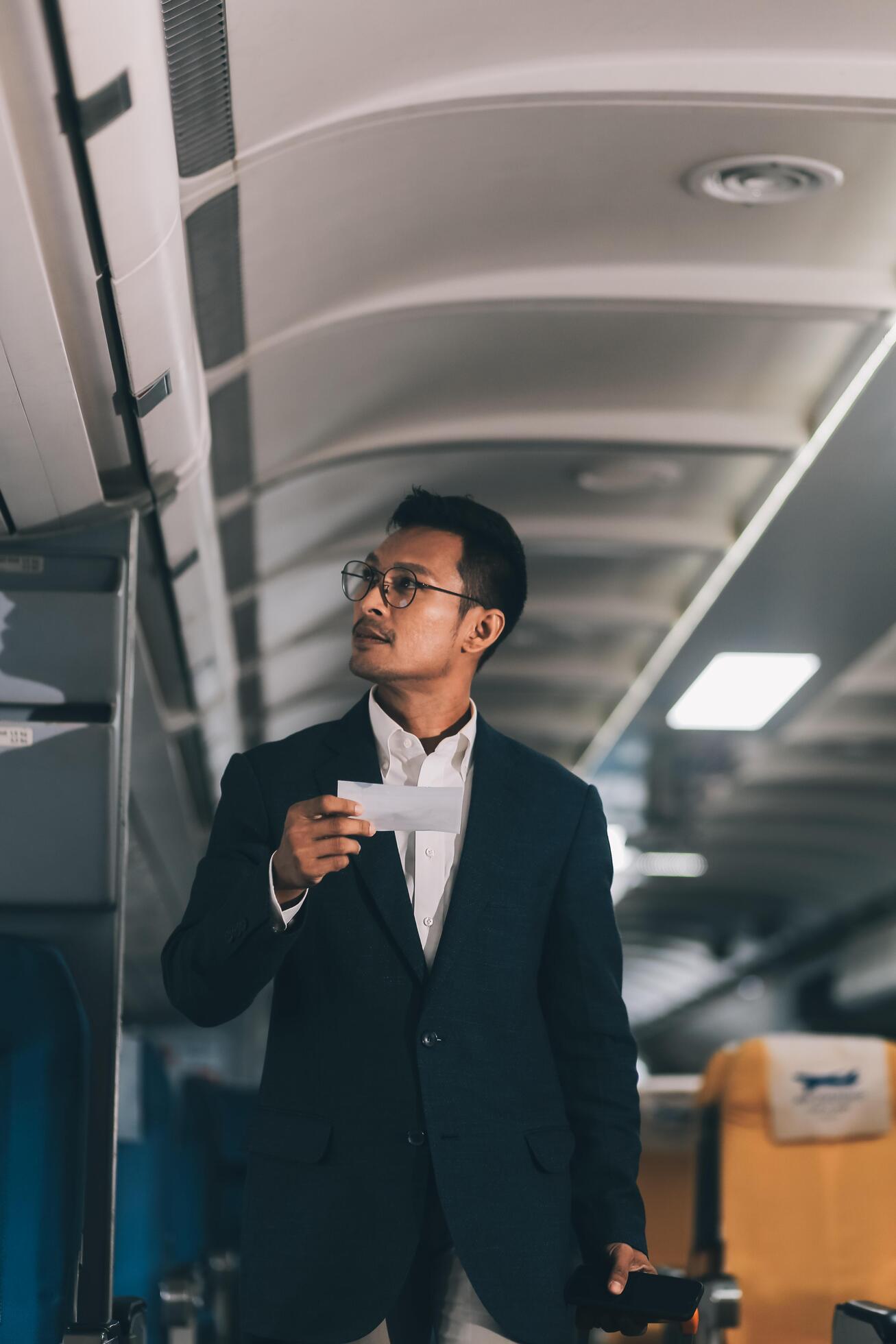 Handsome Asian male passenger takes his carry-on luggage out of the overhead locker after landing at his destination. transportation concept Stock Free