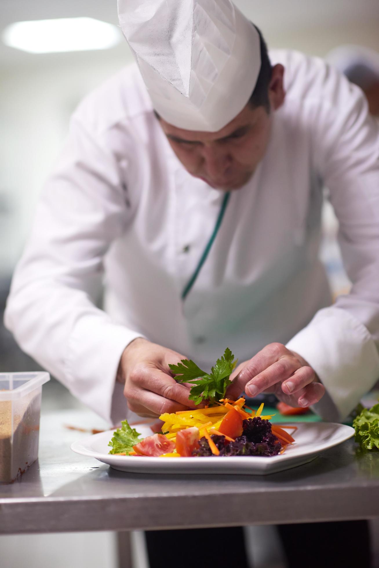 chef in hotel kitchen preparing and decorating food Stock Free