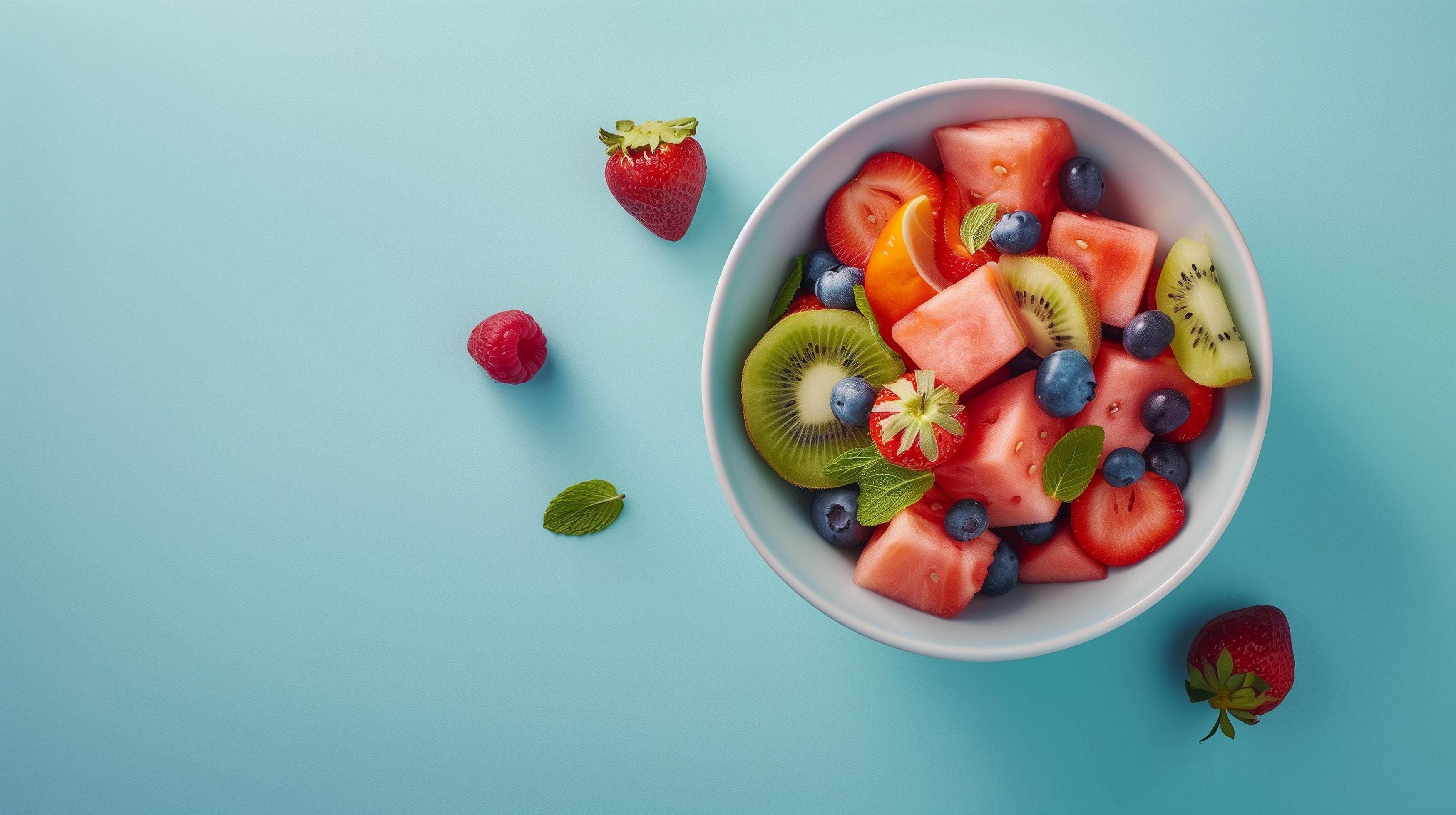 Colorful Fresh Fruit Salad Displayed in a White Bowl Against a Light Blue Background Stock Free