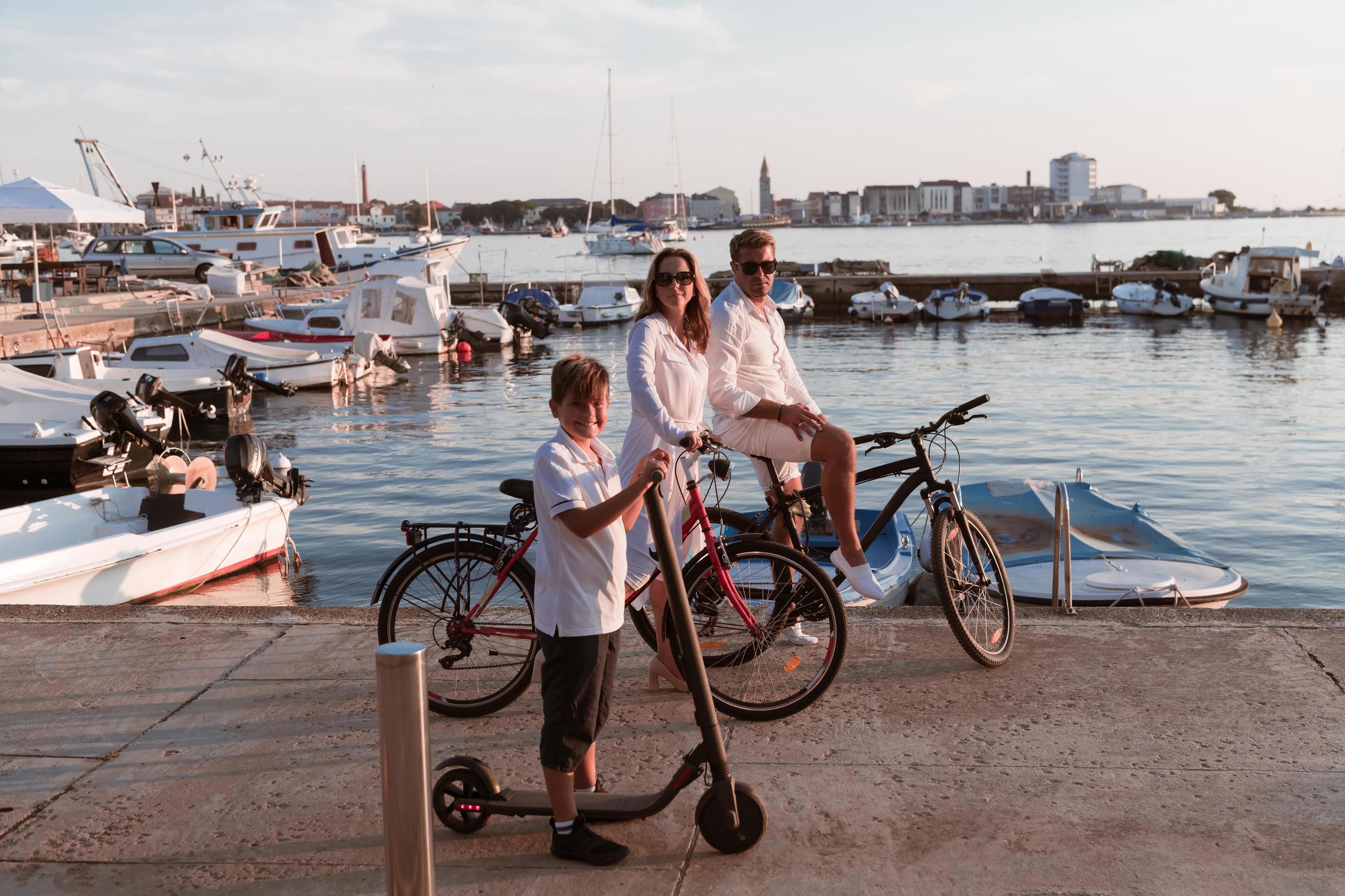 Happy family enjoying a beautiful morning by the sea together, parents riding a bike and their son riding an electric scooter. Selective focus Stock Free