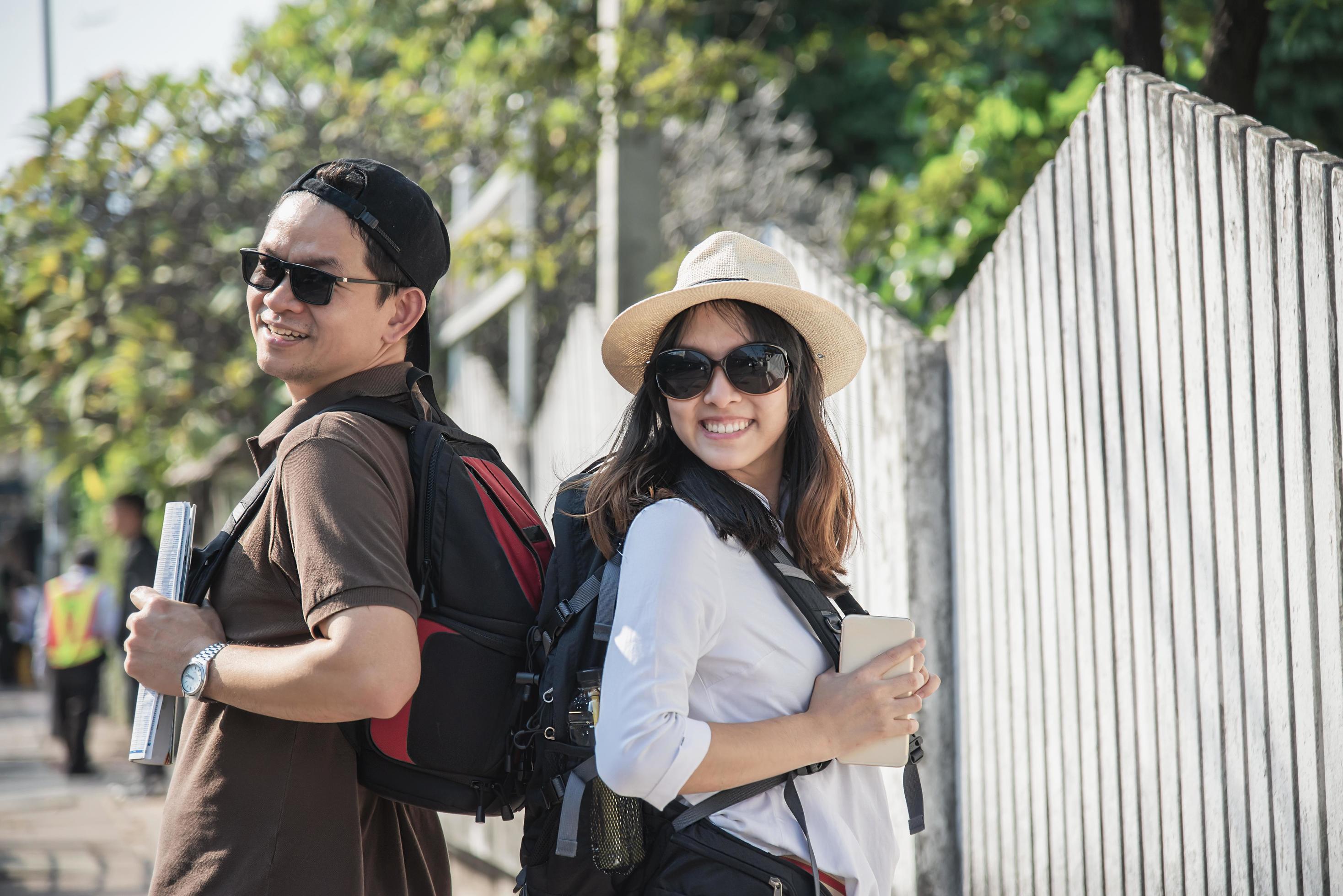 Asian backpack couple tourist holding city map crossing the road – travel people vacation lifestyle concept Stock Free