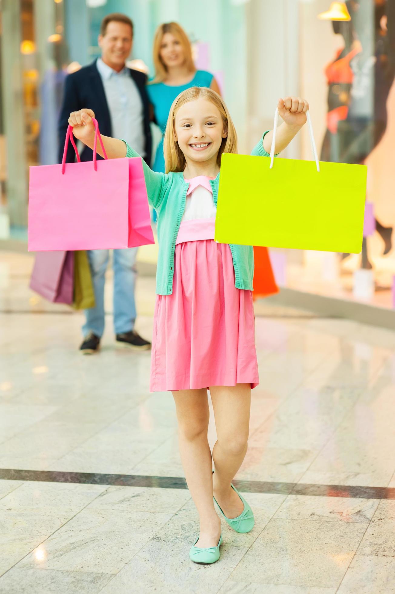 Family shopping. Cheerful family shopping in shopping mall while little girl showing her shopping bags and smiling Stock Free