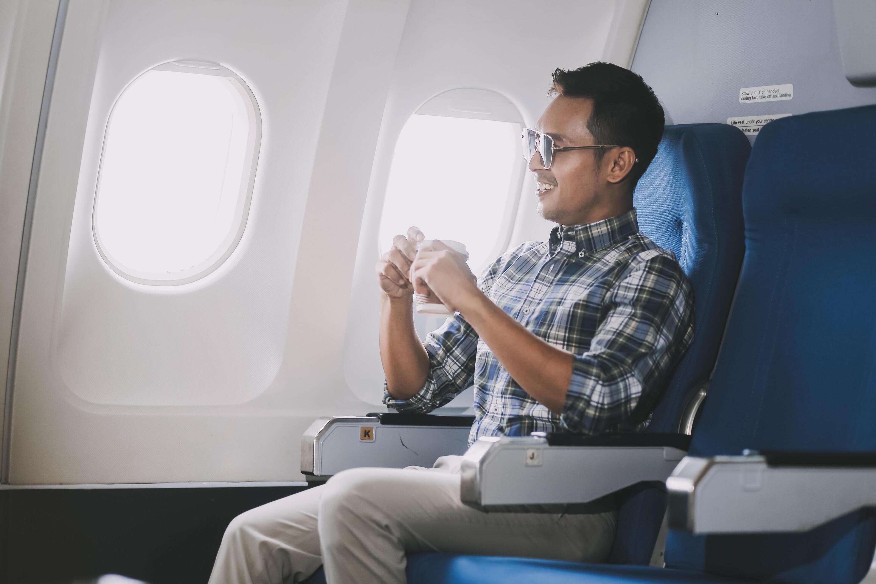 Asian man enjoying enjoys a coffee comfortable flight while sitting in the airplane cabin, Passengers near the window. Stock Free