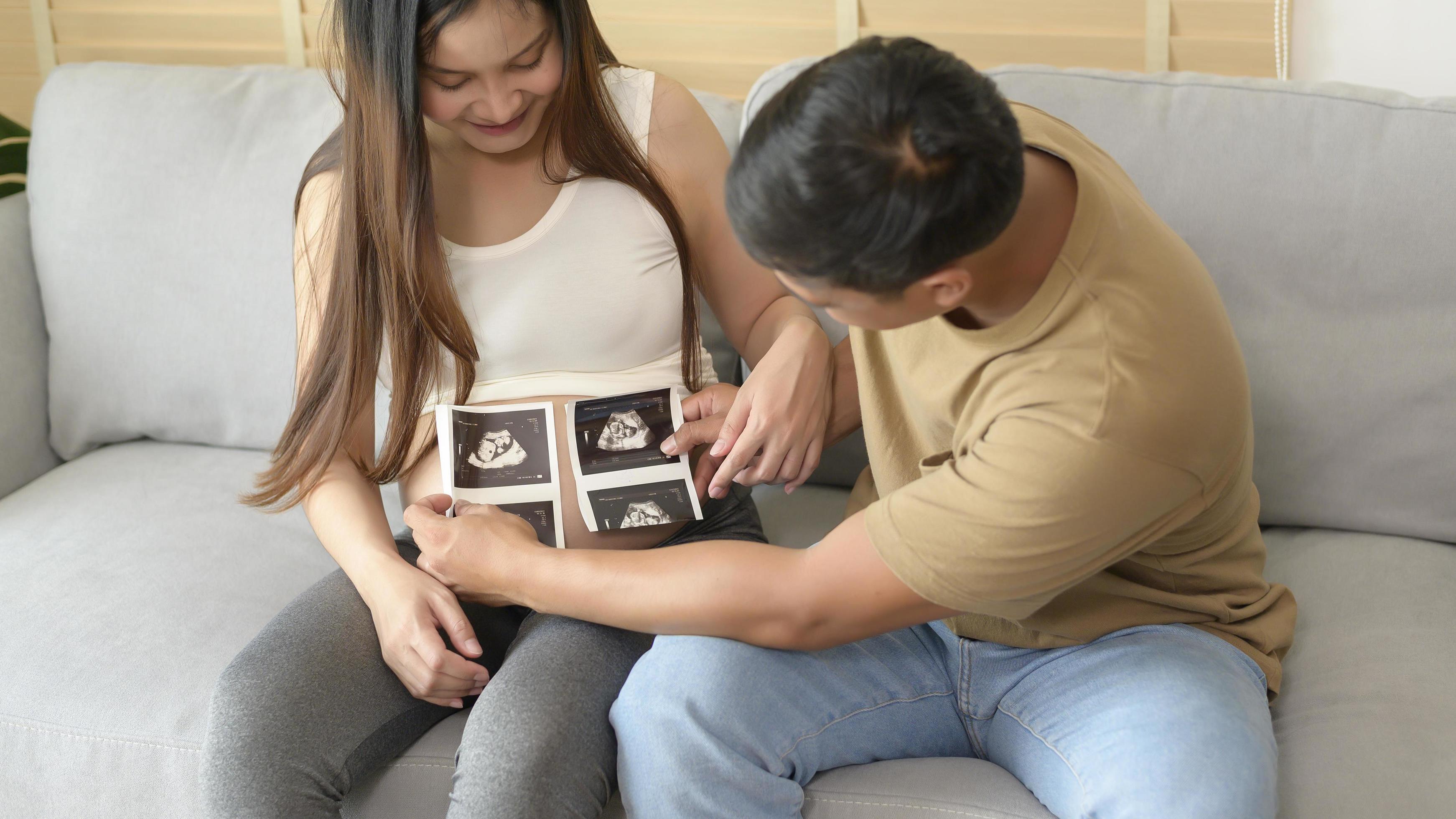 Young pregnant woman with husband holding ultrasound photo of newborn baby, maternity and family concept Stock Free