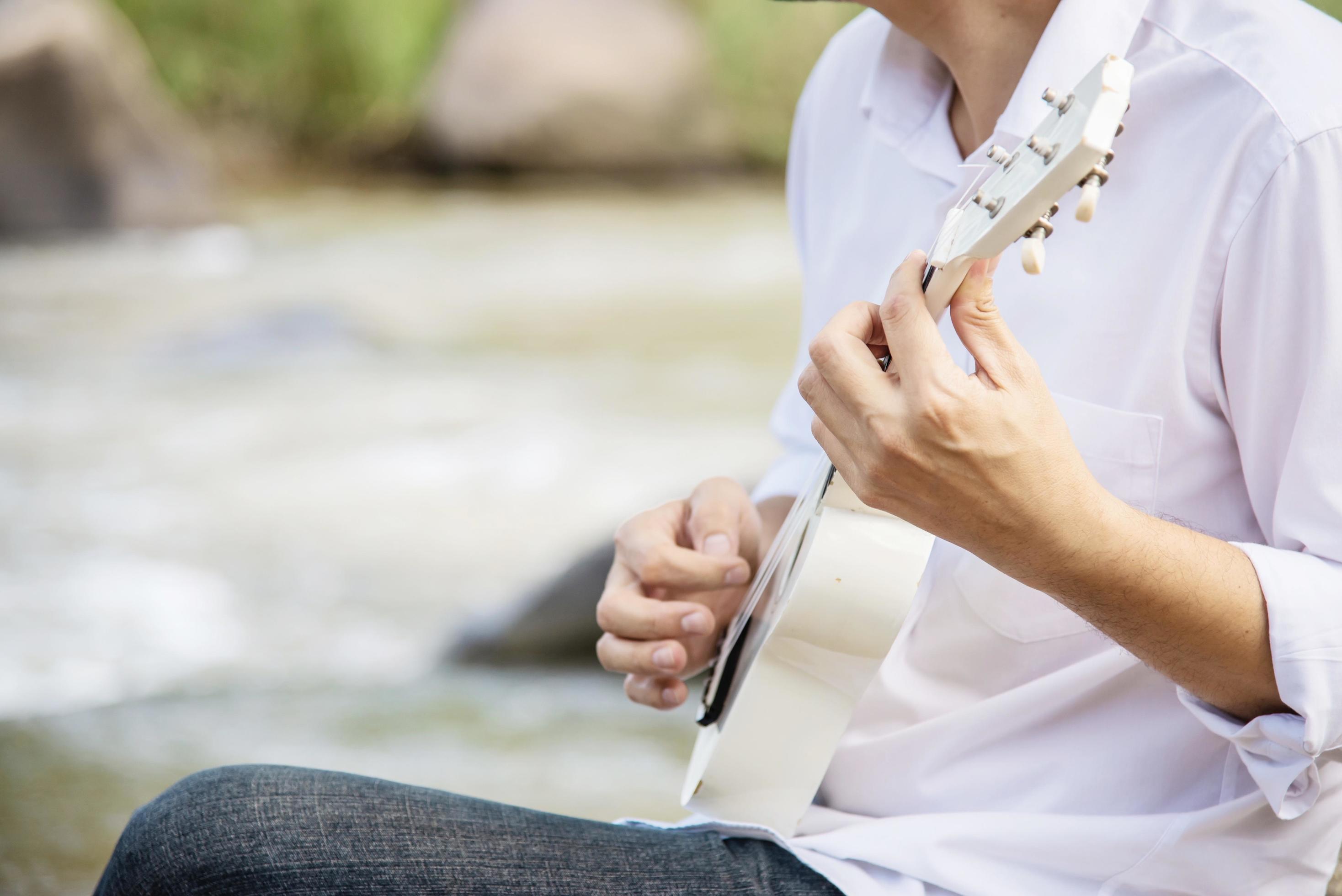 Man play ukulele new to the river- people and music instrument life style in nature concept Stock Free