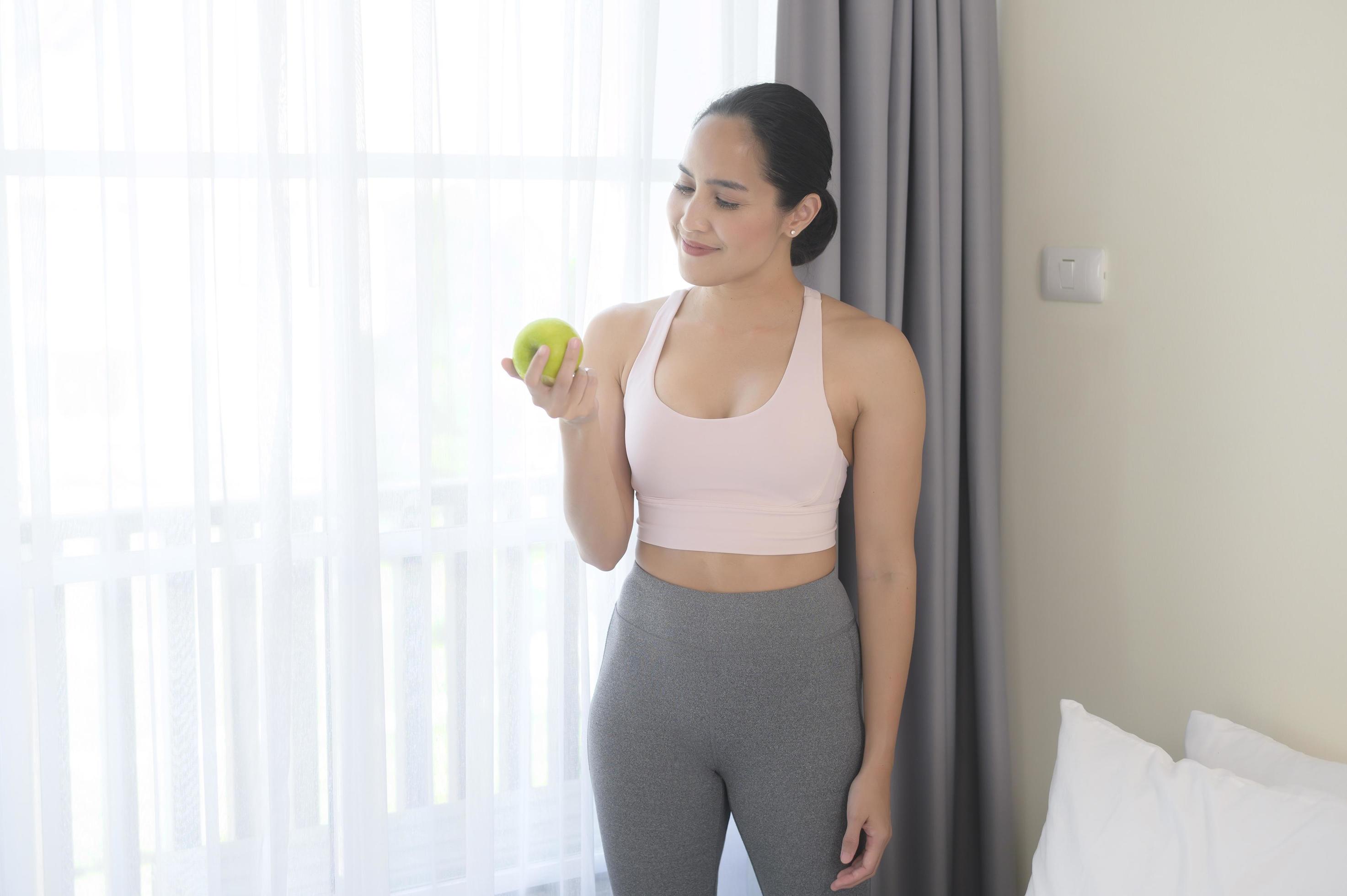 Fit young woman eating an apple after work out at home, sport and healthy lifestyle concept. Stock Free