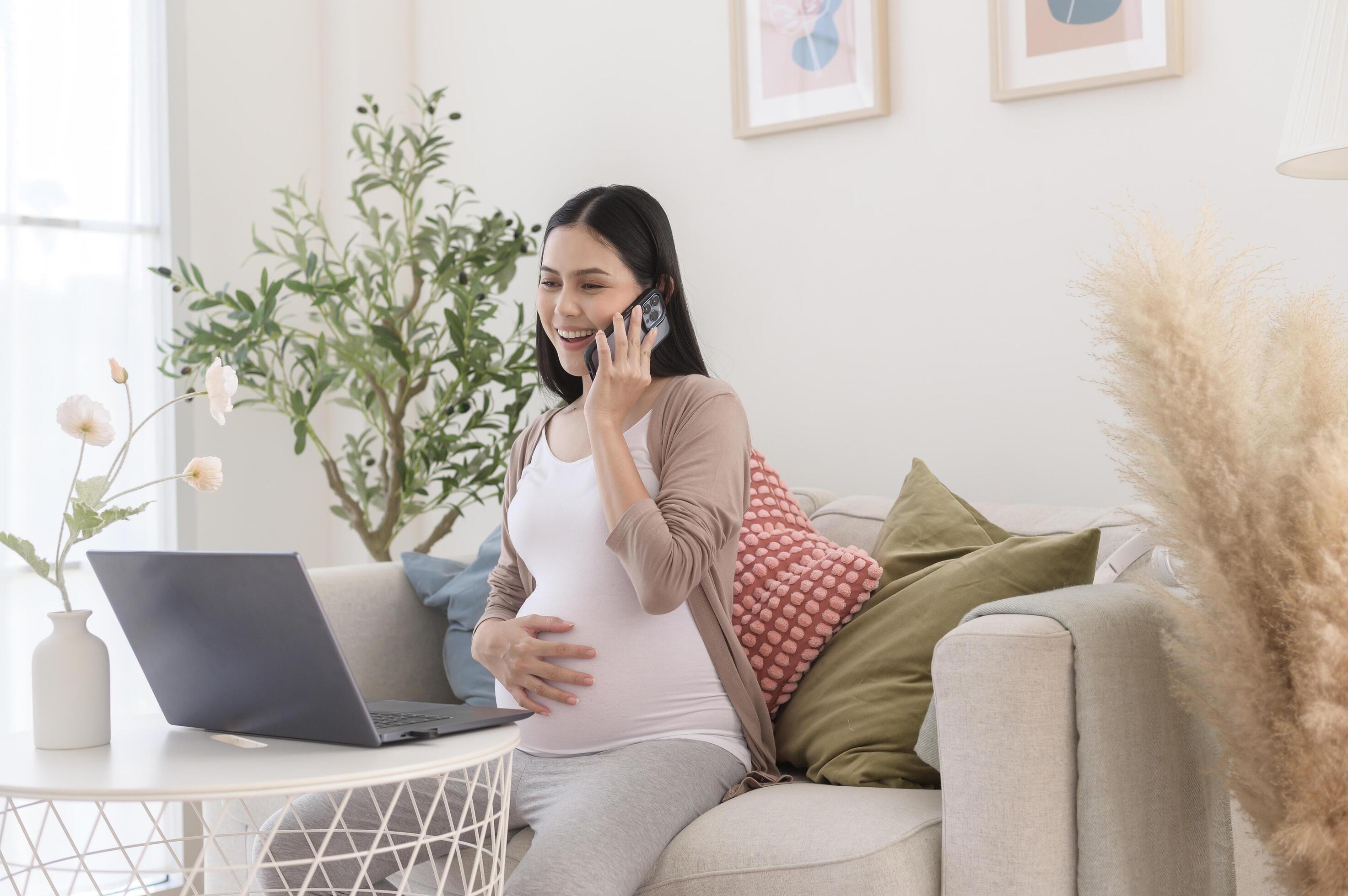 Pregnant woman working on laptop and smart phone in the living room at home Stock Free