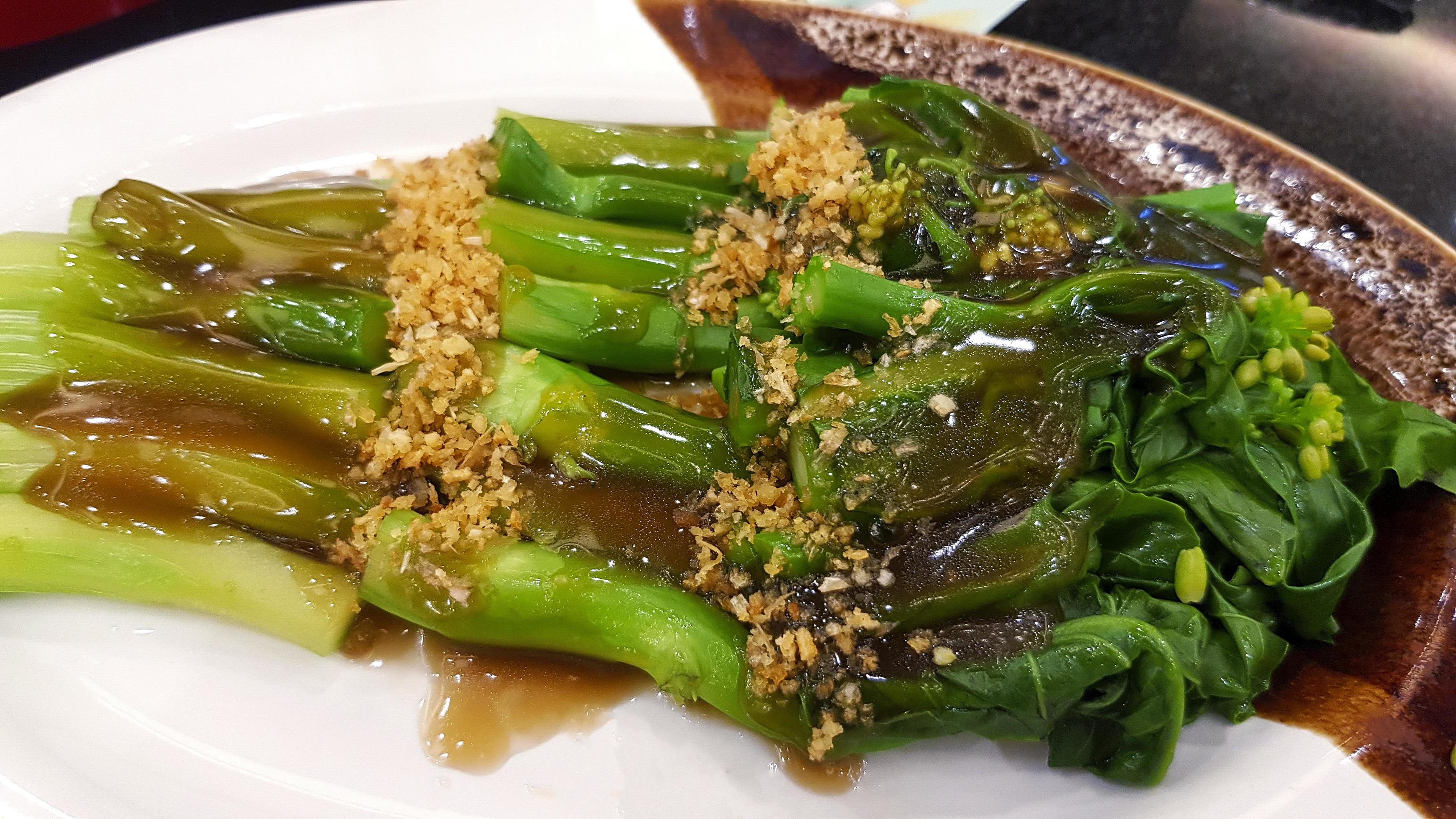 Hong Kong kale with oyster sauce and dried garlic topping on white dish or plate at Chinese restaurant. Delicious Asian food. Stock Free