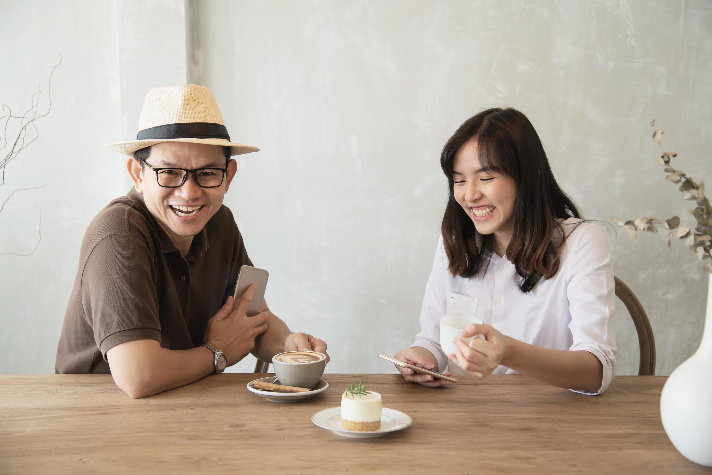 Casual man and woman talking happily while drink coffee and looking mobile phone – happy time lifestyle in coffee shop Stock Free