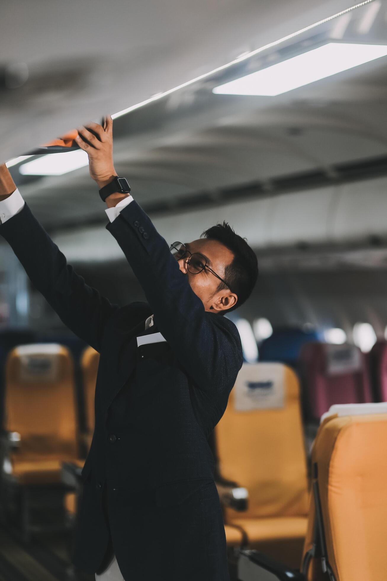 Handsome Asian male passenger takes his carry-on luggage out of the overhead locker after landing at his destination. transportation concept Stock Free