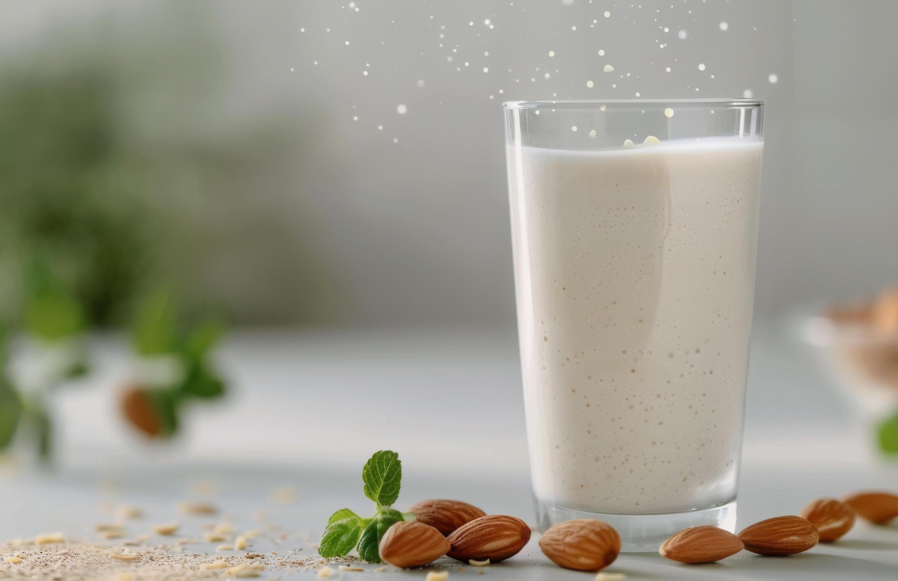 Creamy Almond Milk Surrounded by Almonds and Fresh Leaves on a White Background Stock Free