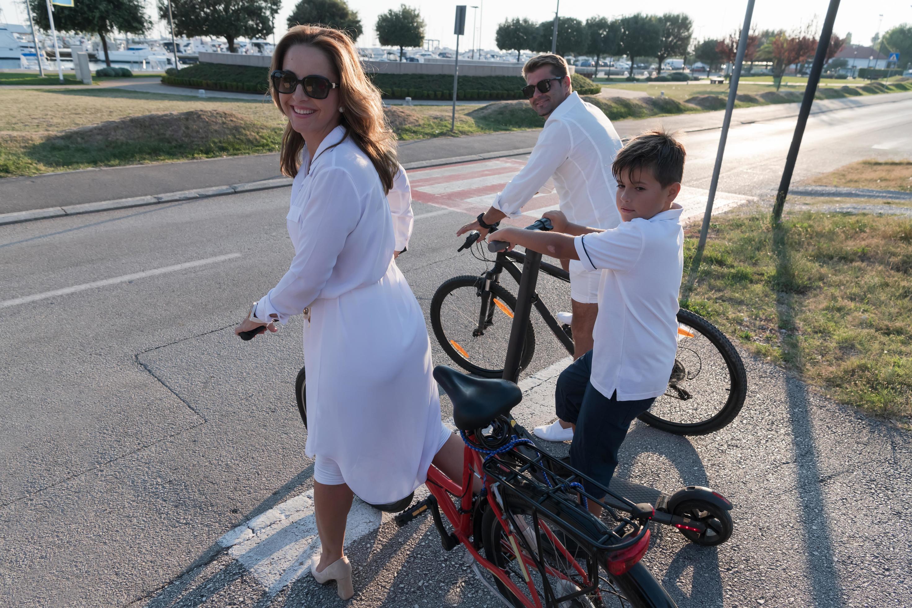 Happy family enjoying a beautiful morning by the sea together, parents riding a bike and their son riding an electric scooter. Selective focus Stock Free