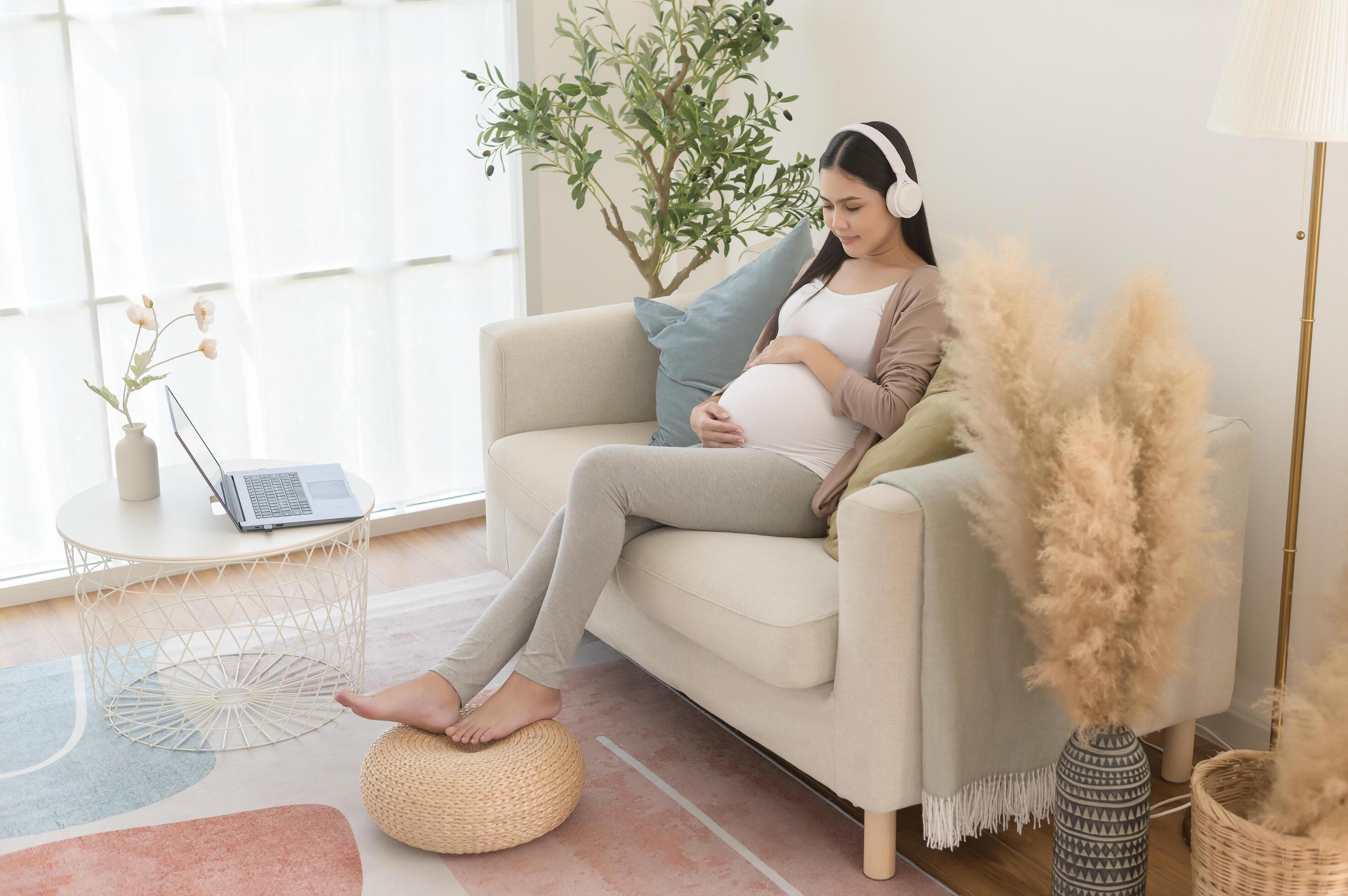 Happy pregnant woman with headphones listening to mozart music and lying on sofa, pregnancy concept Stock Free