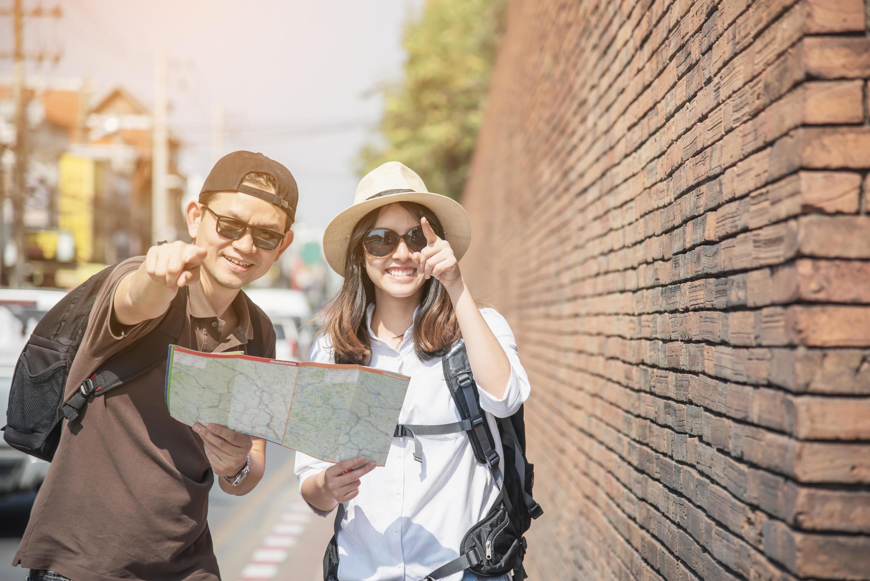 Asian backpack couple tourist holding city map crossing the road – travel people vacation lifestyle concept Stock Free