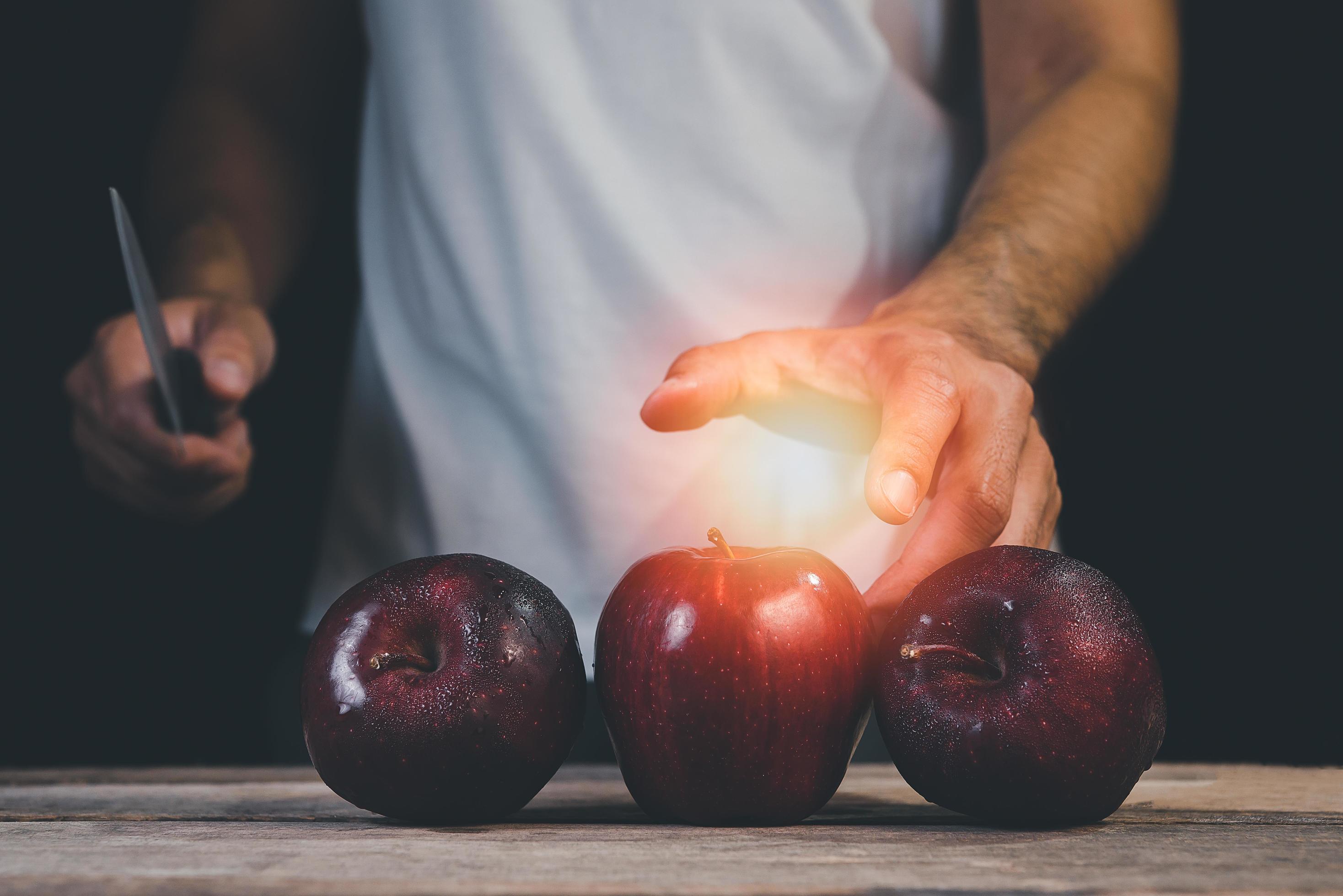 Man hand holding knife prepare to cut red apple on wood table and dark background. Fruits and food concept. Stock Free