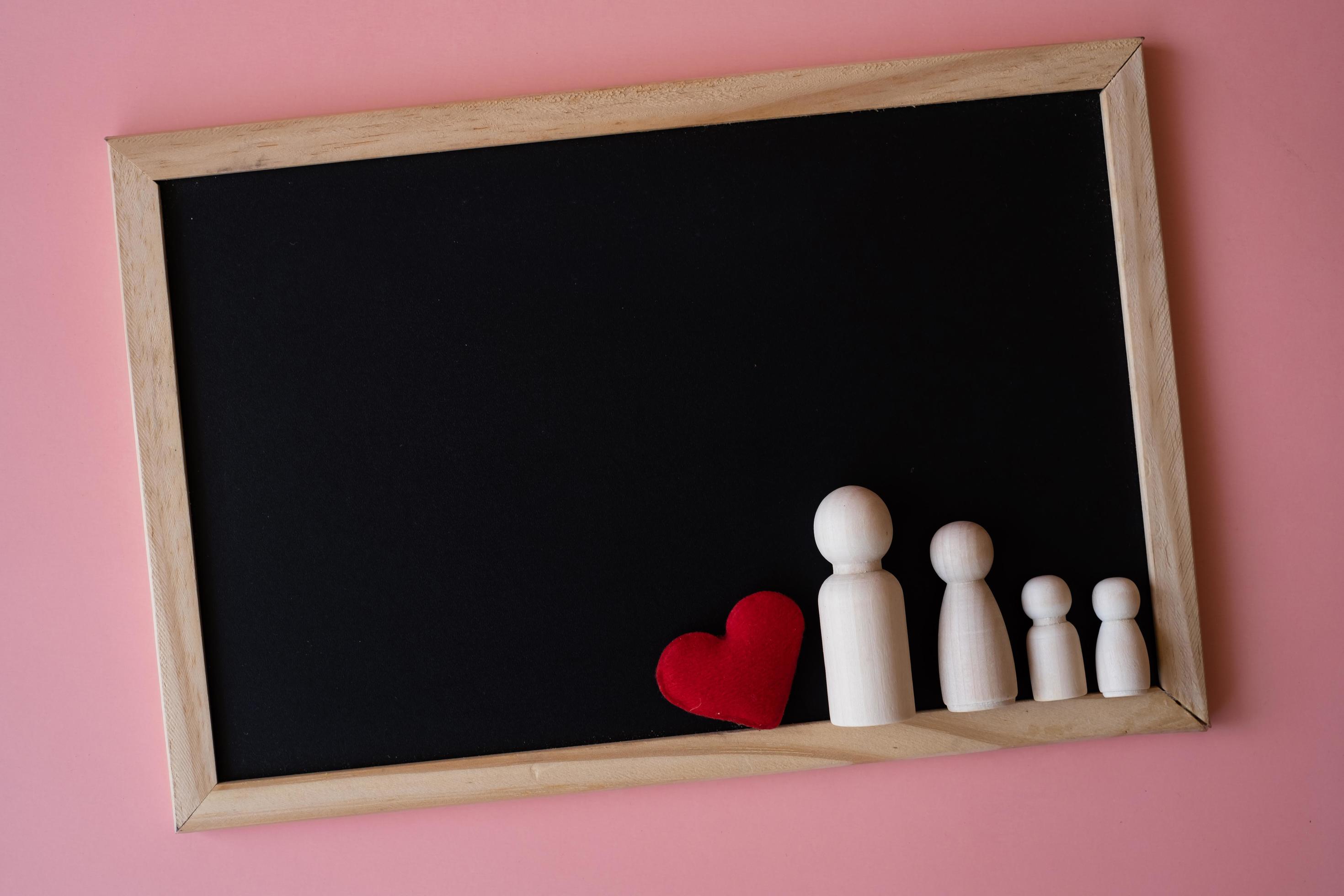 Wooden figurines of family father, mother and children on the black board on pink background. copy space for text. Stock Free