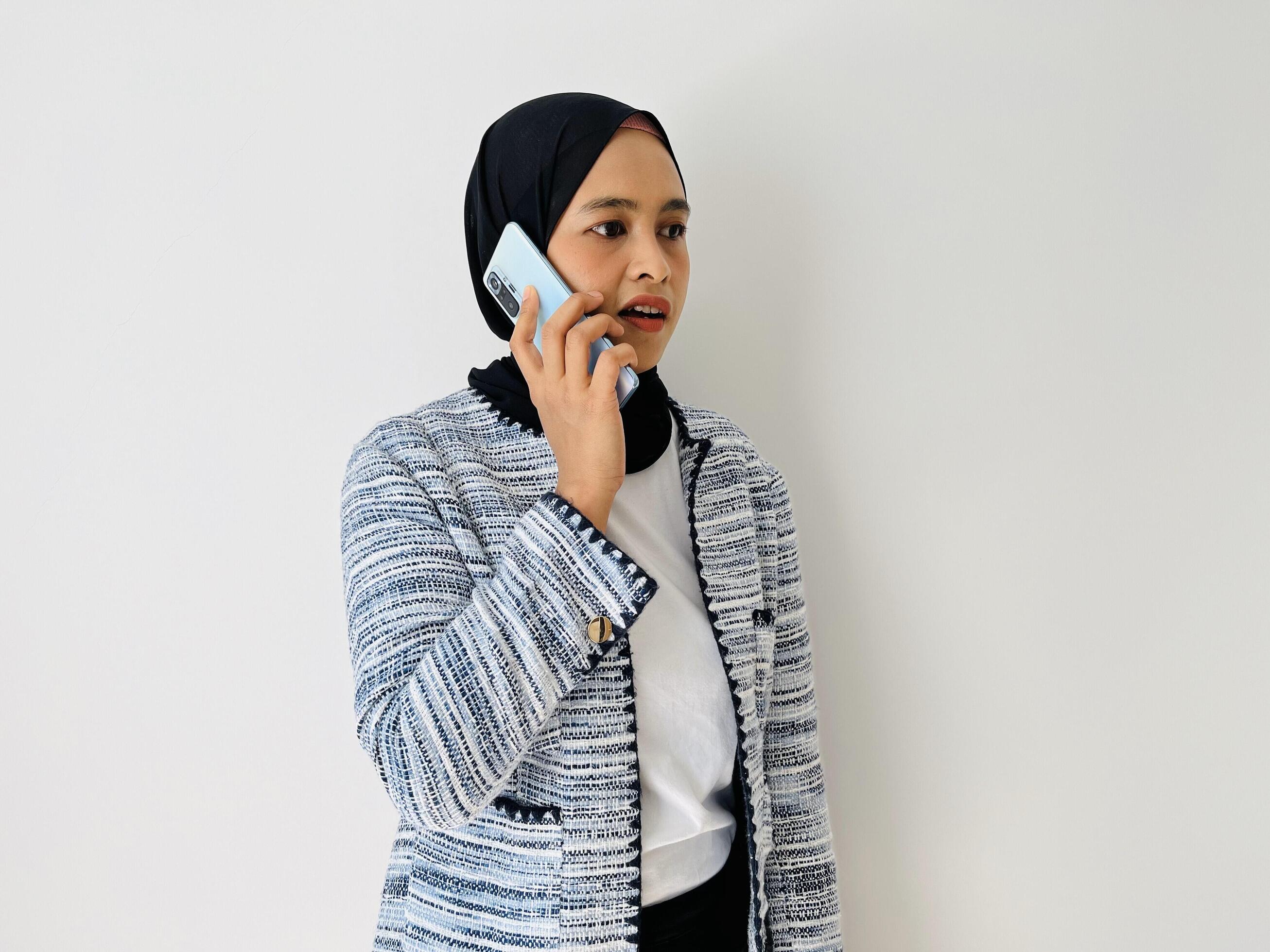 Young Asian woman using mobile phone having call. Standing female wearing black hijab and tweed blazer isolated on white background. Stock Free