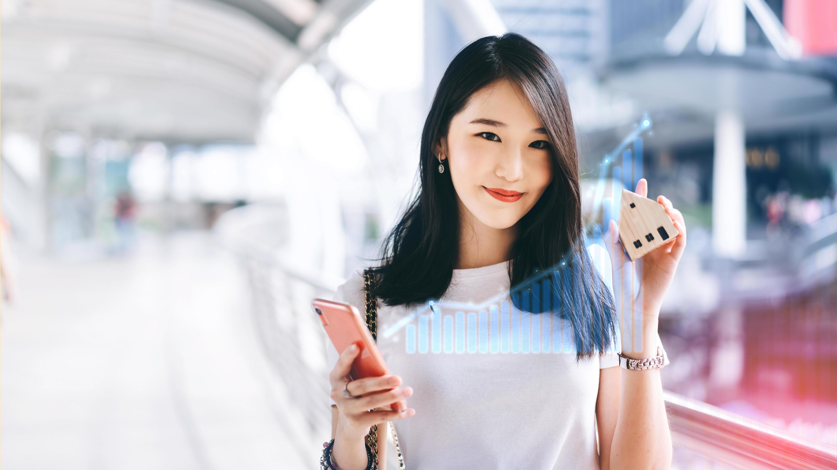 Young adult business working asian woman holding mobile phone and house model for online insurance application with digital finance graph. Stock Free