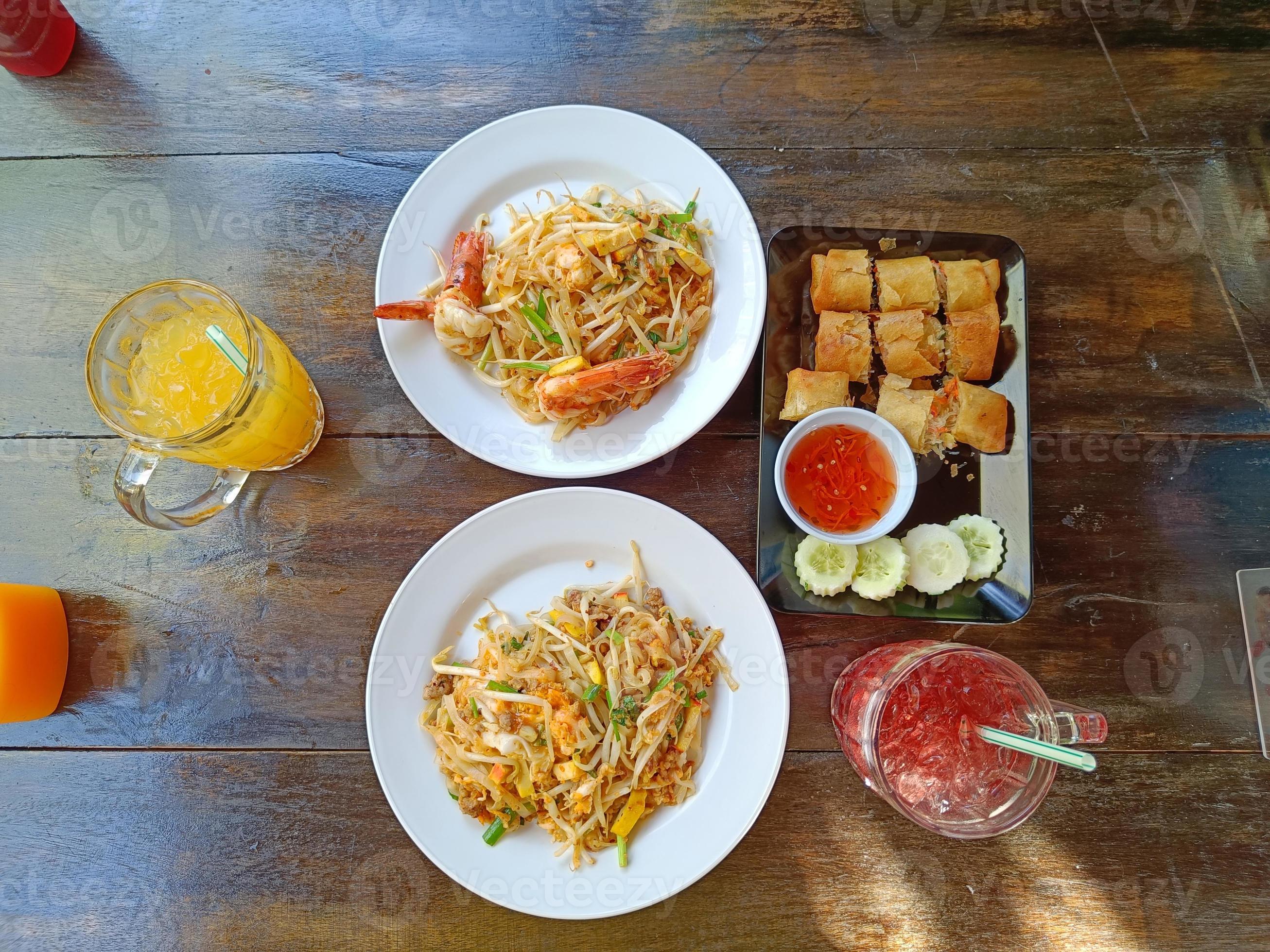 Pad Thai on the table served with orange juice, Roselle juice and fried spring rolls. popular Thai food, Top view Stock Free