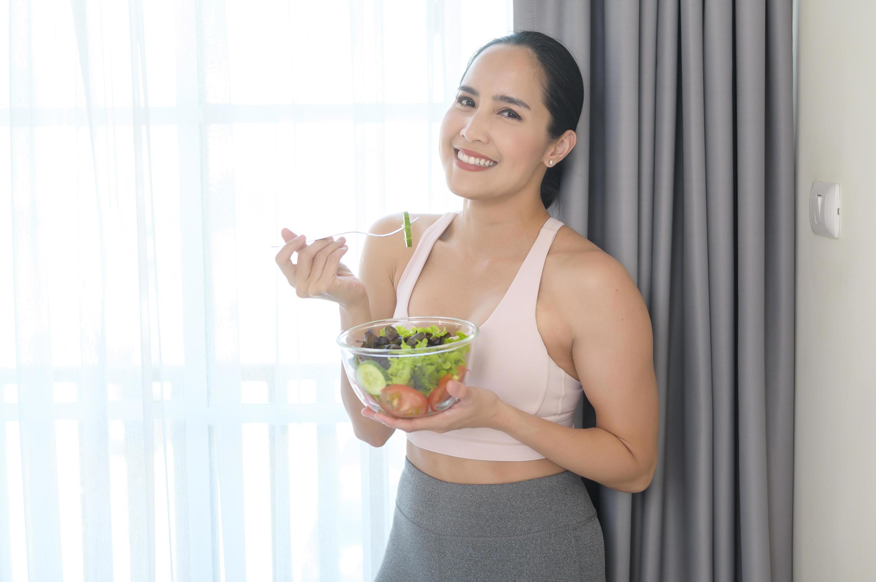 Fit young woman having salad after work out at home, sport and healthy lifestyle concept. Stock Free