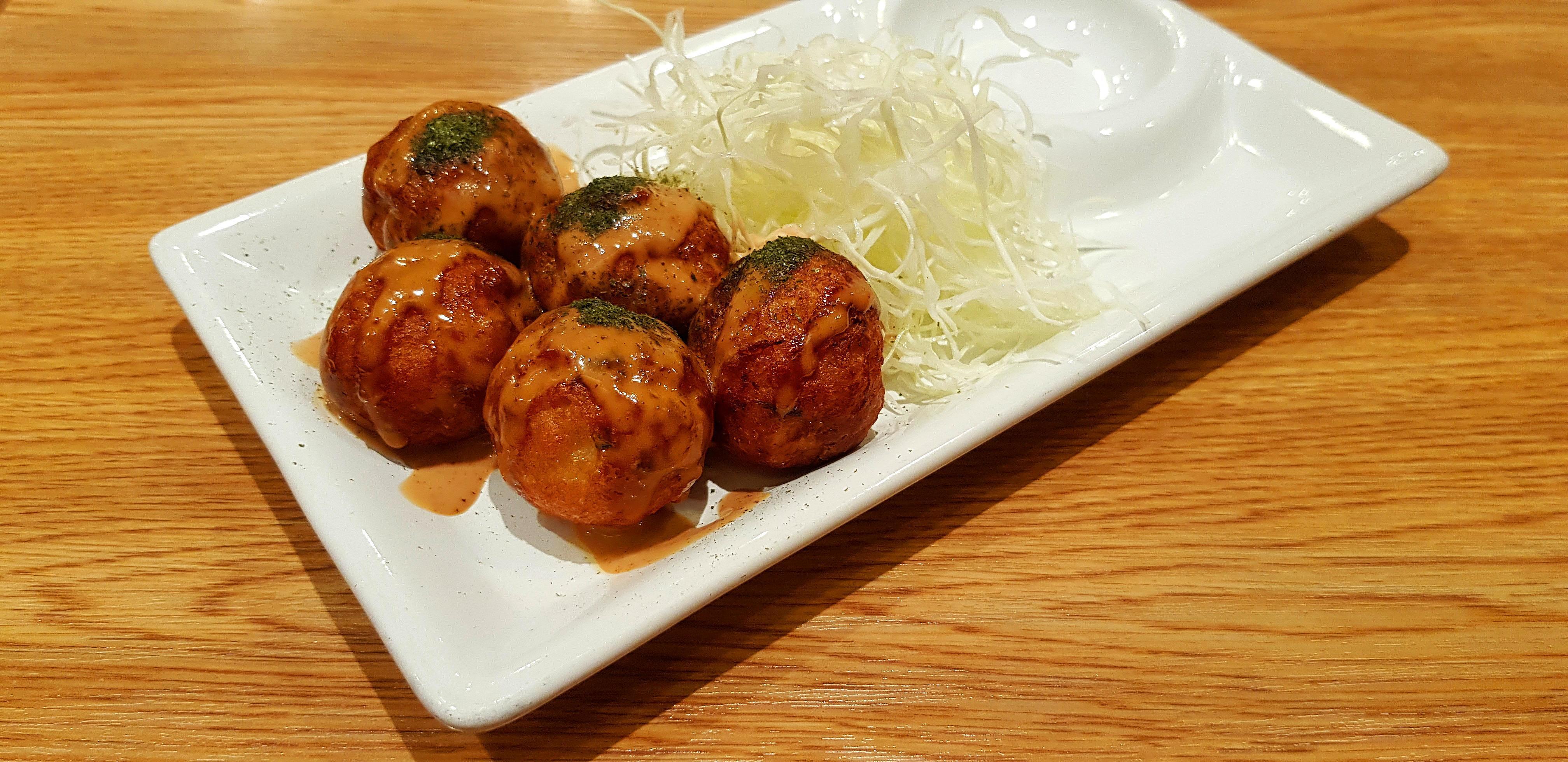 Takoyaki topped with sweet sauce and sliced cabbage in white dish on brown wooden background. Japanese food in plate on wood table with copy space. Stock Free