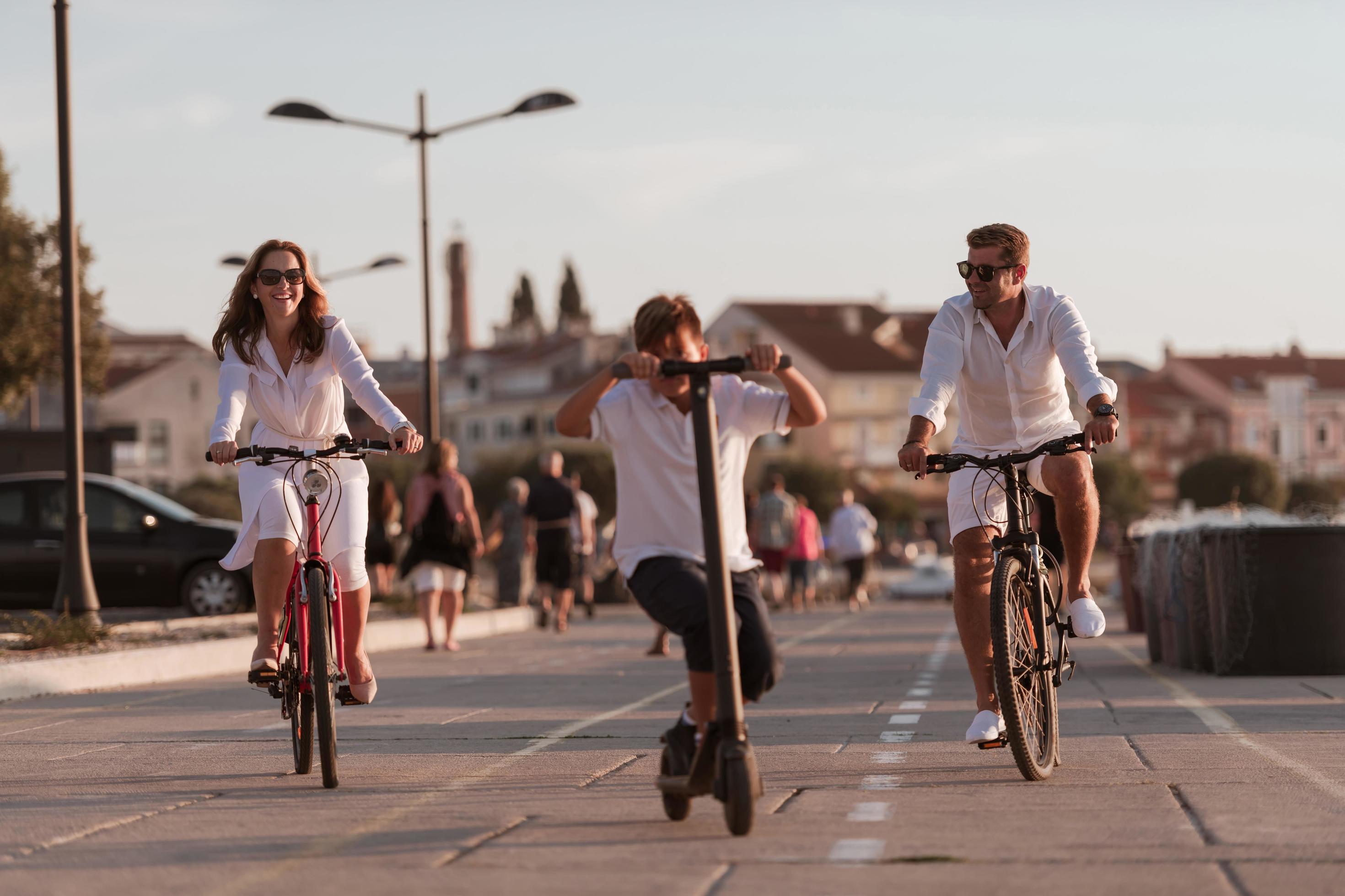 Happy family enjoying a beautiful morning by the sea together, parents riding a bike and their son riding an electric scooter. Selective focus Stock Free