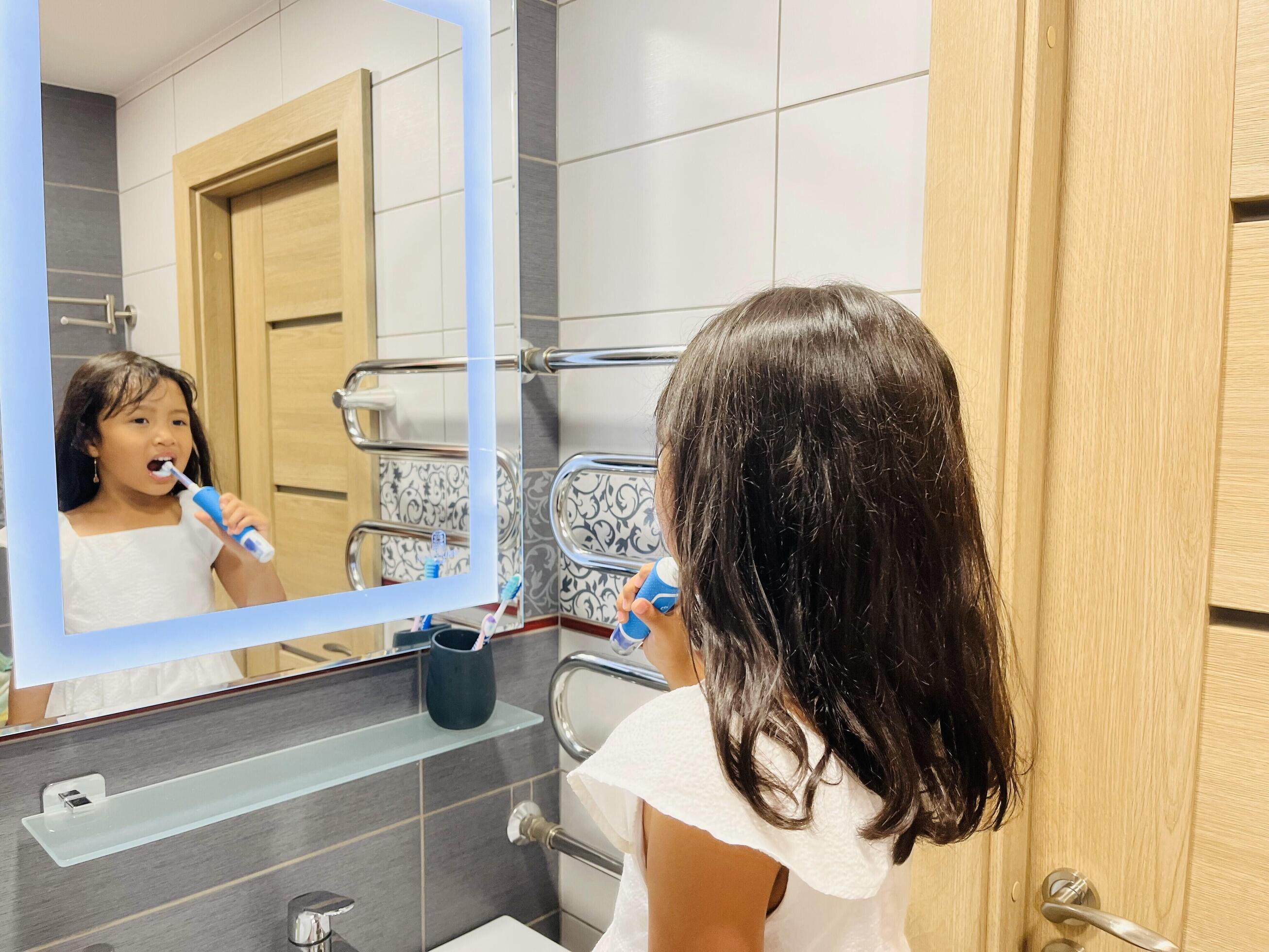 A happy little Asian girl brushes her teeth in front of a mirror in the bathroom. Morning routine. Hygiene Stock Free