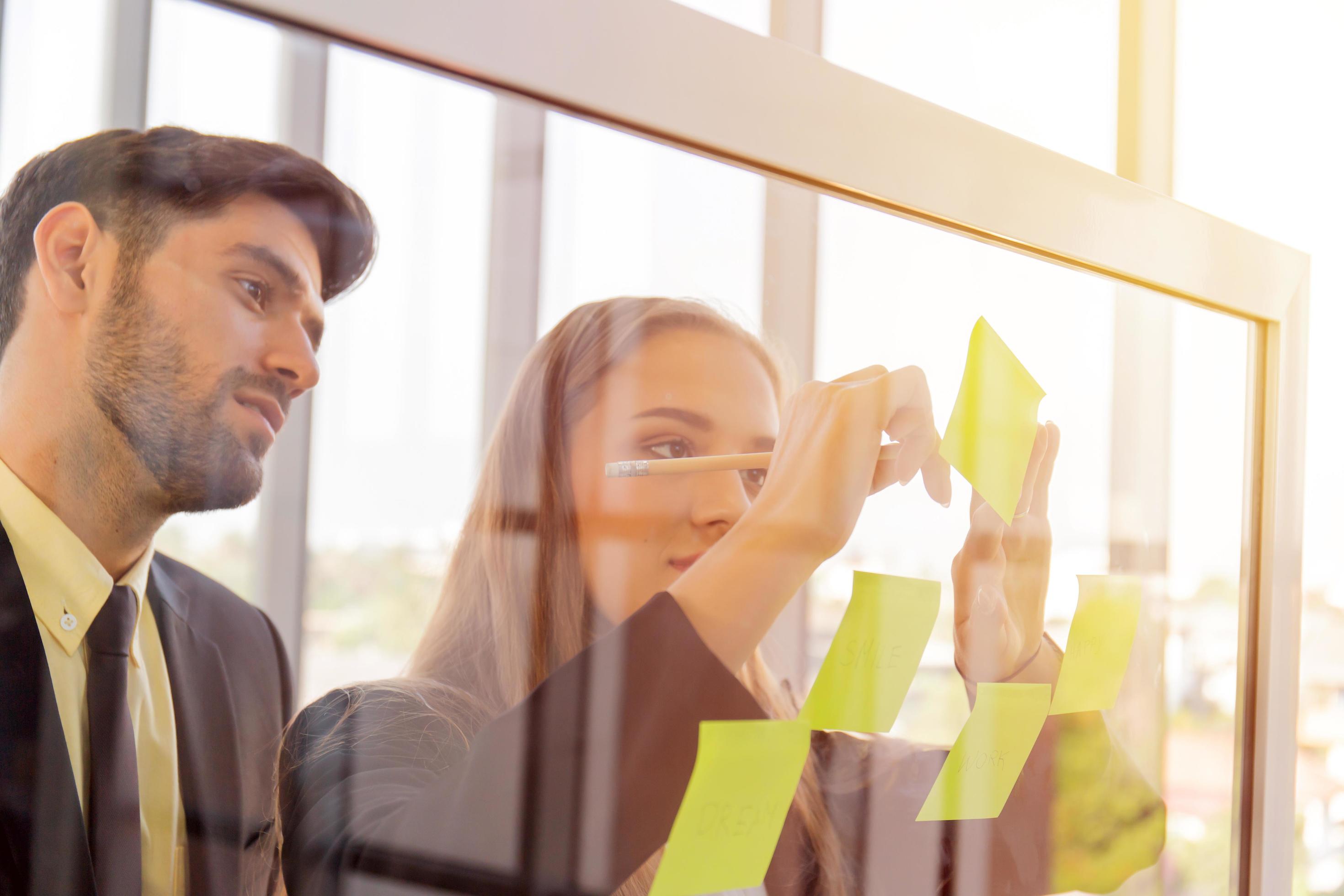 Two business men and women put notes on clear glass and have a beautiful orange light. Stock Free